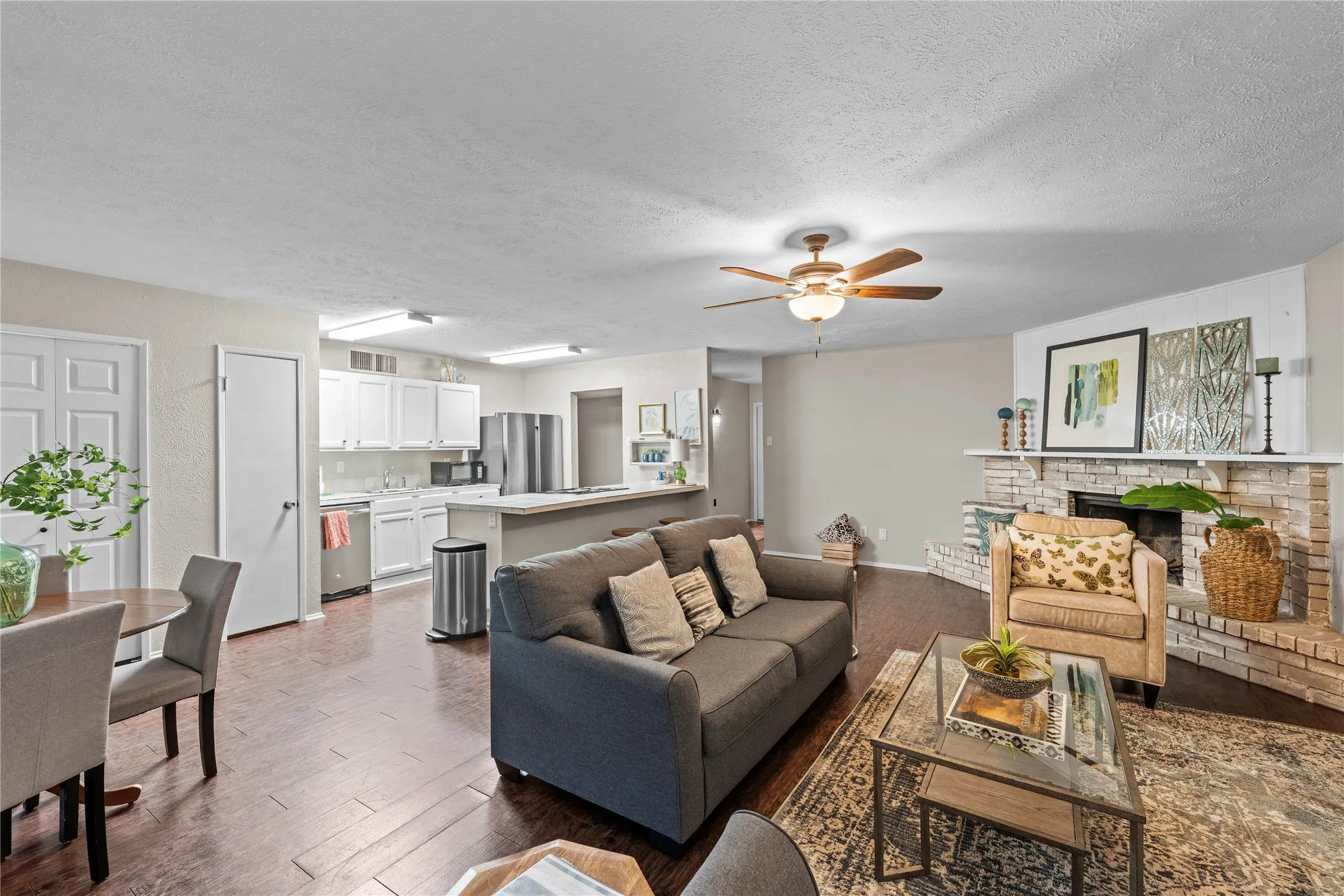 Open-concept living area featuring wood-finish flooring, a brick fireplace with mantel, and ceiling fan