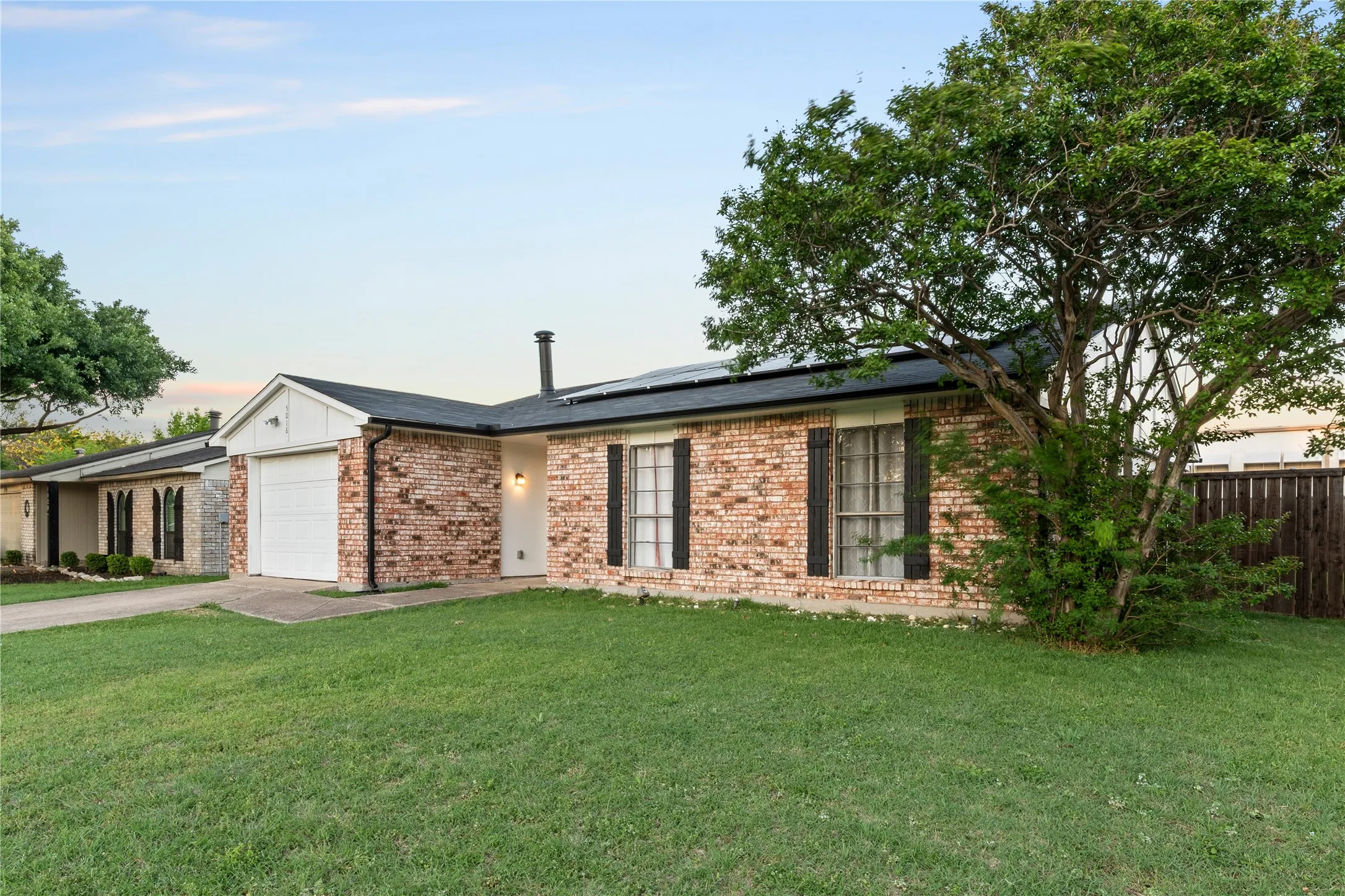 Brick facade, dark shingle roof, attached garage, exterior wall lantern, and solar panels