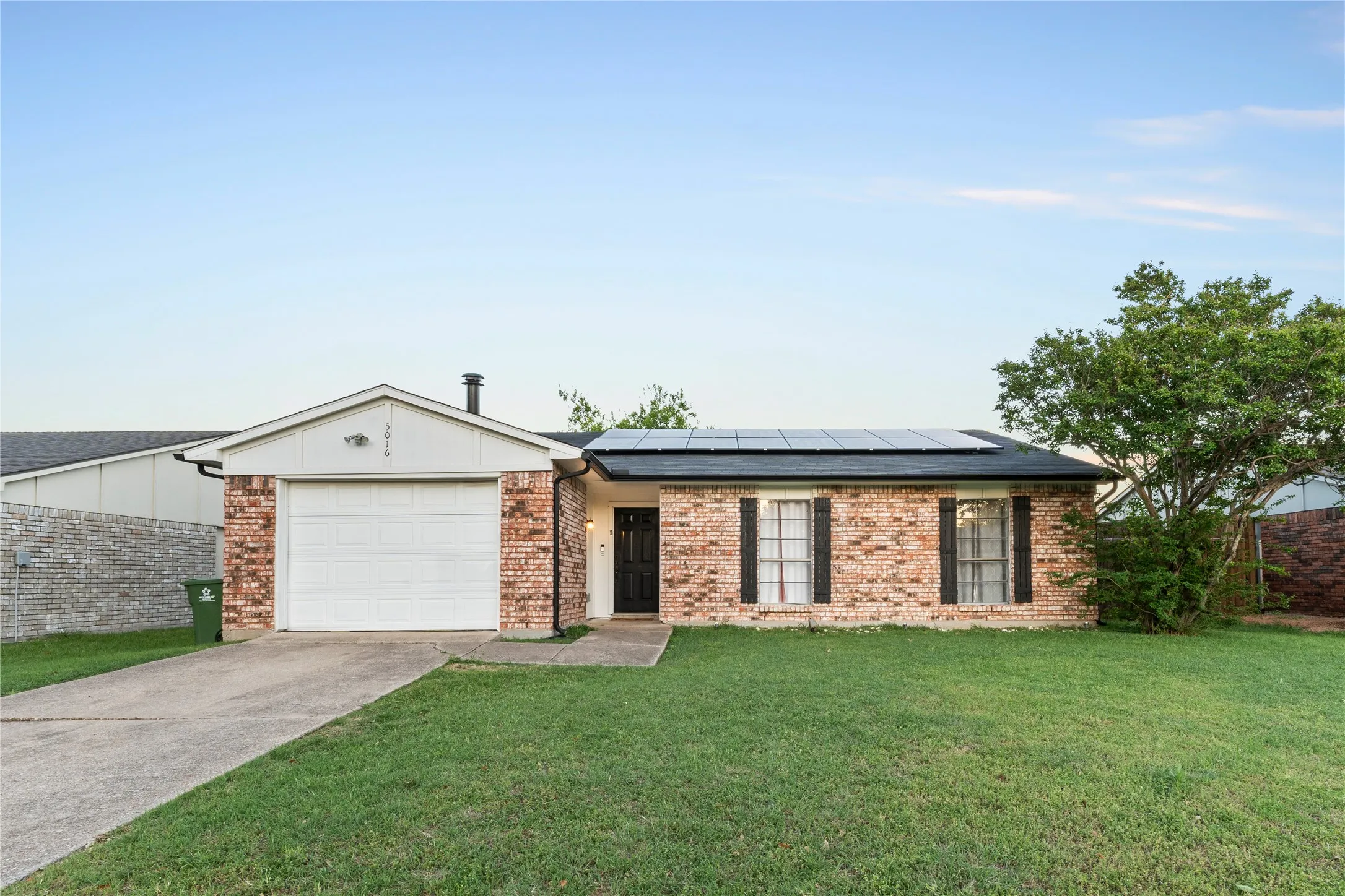 Brick exterior with dark shutters, attached garage, concrete driveway, and solar panels