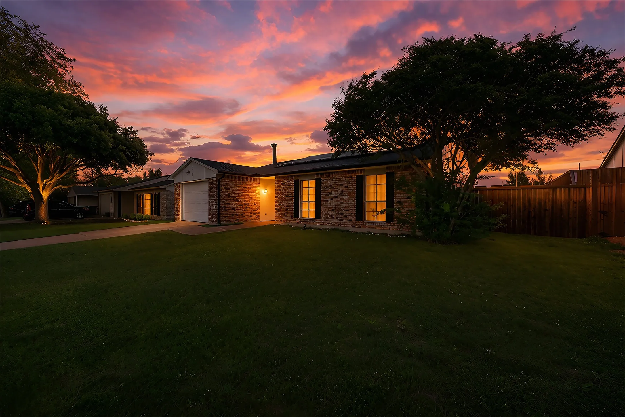 Brick exterior with a single-car garage, mature trees, and a spacious lawn