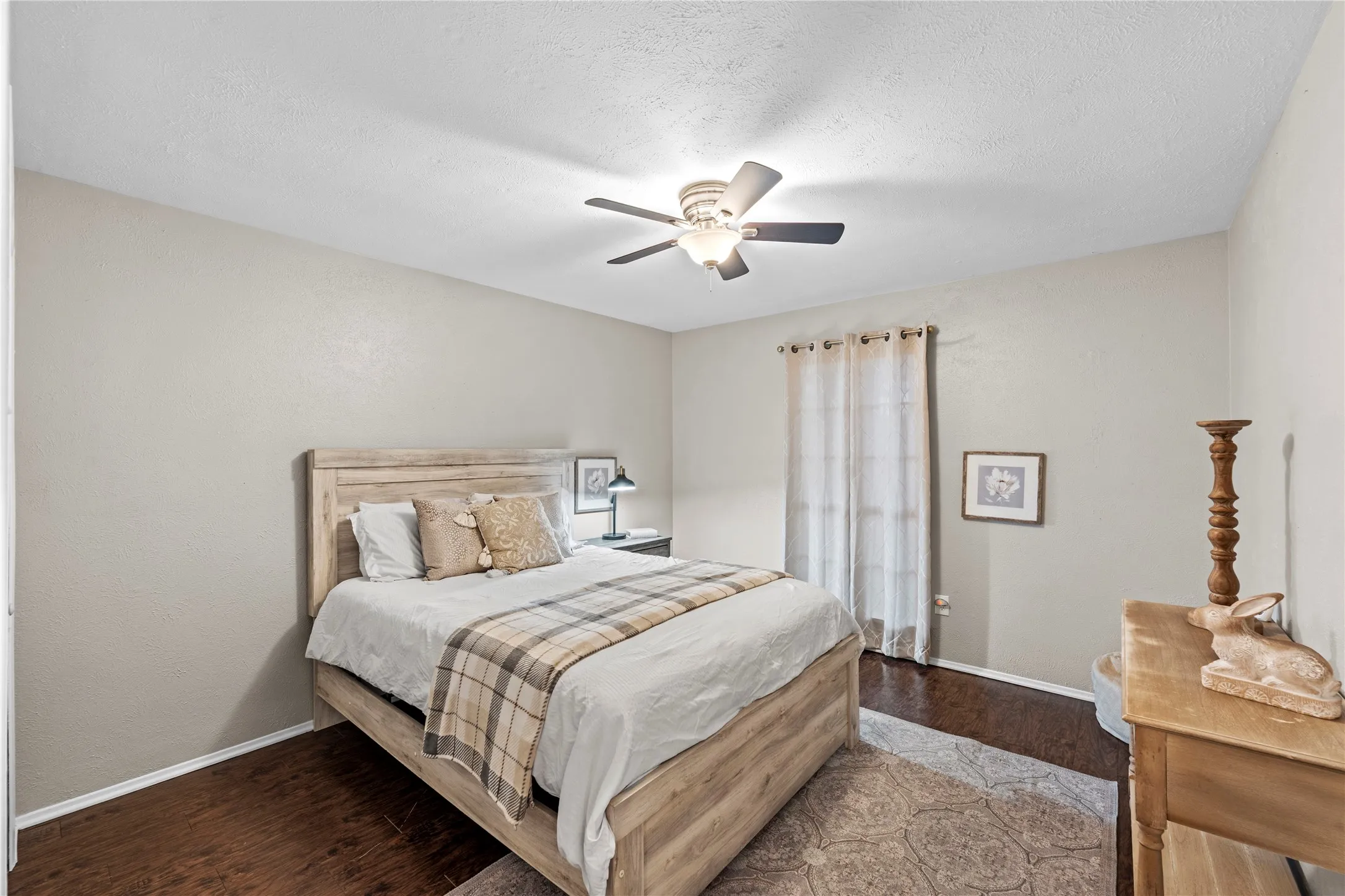 Wood-finish flooring, ceiling fan with integrated lighting, window with curtains, and neutral wall paint
