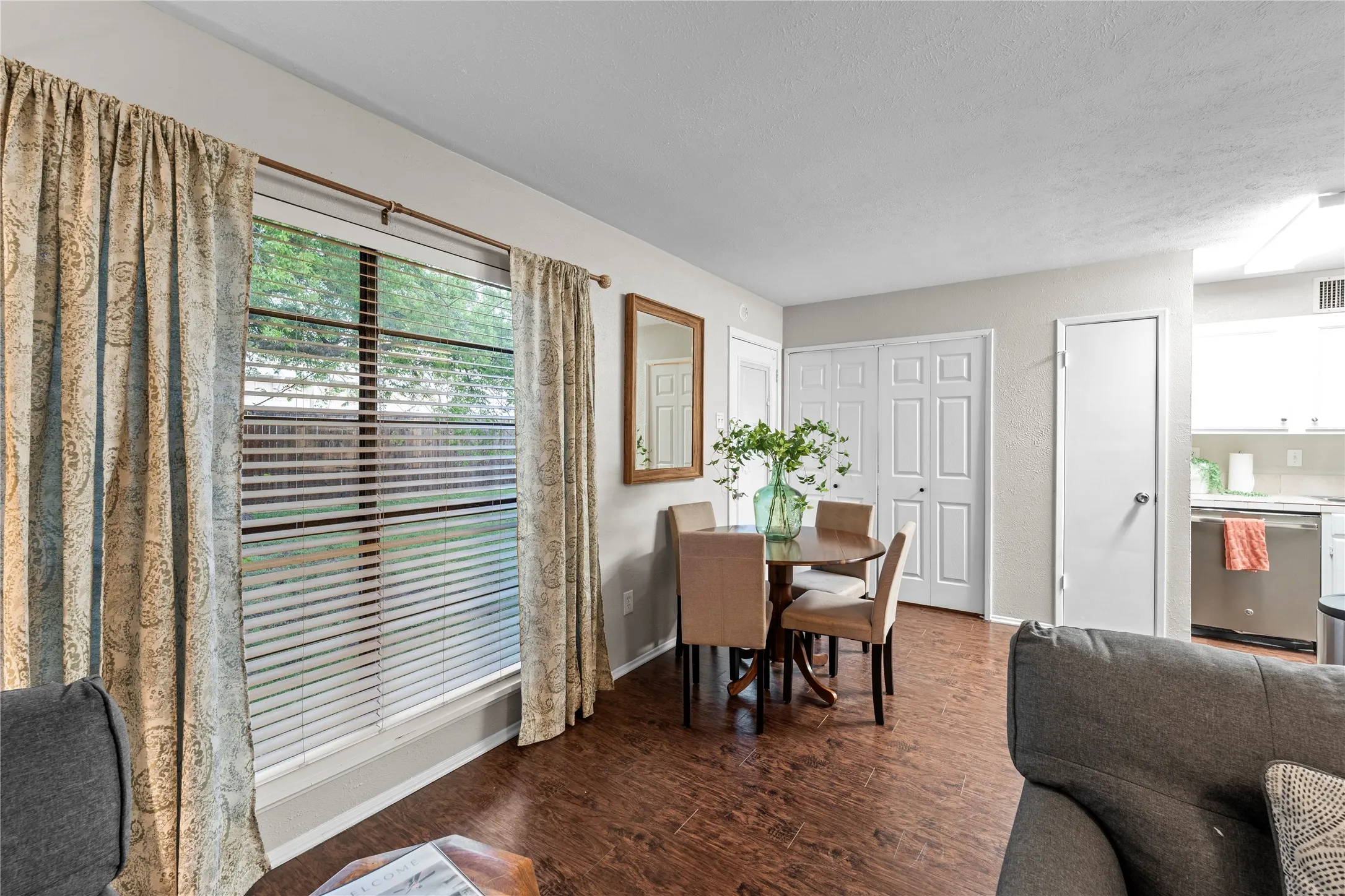 Wood-finish flooring throughout, bright window with horizontal blinds, built-in bi-fold closet doors, and recessed kitchen area