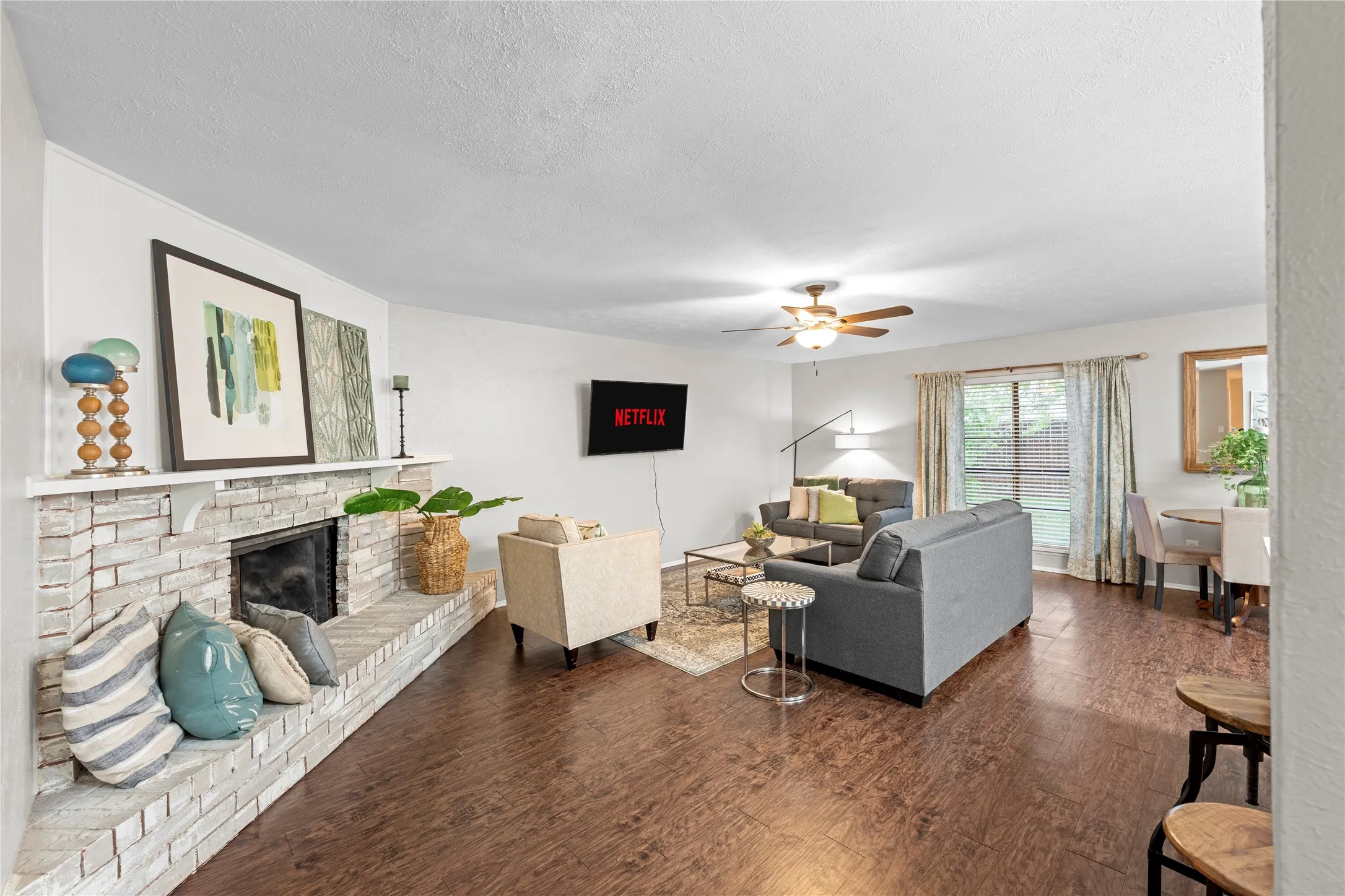 Spacious living area featuring wood-finish flooring, a white brick fireplace with a hearth, and a ceiling fan