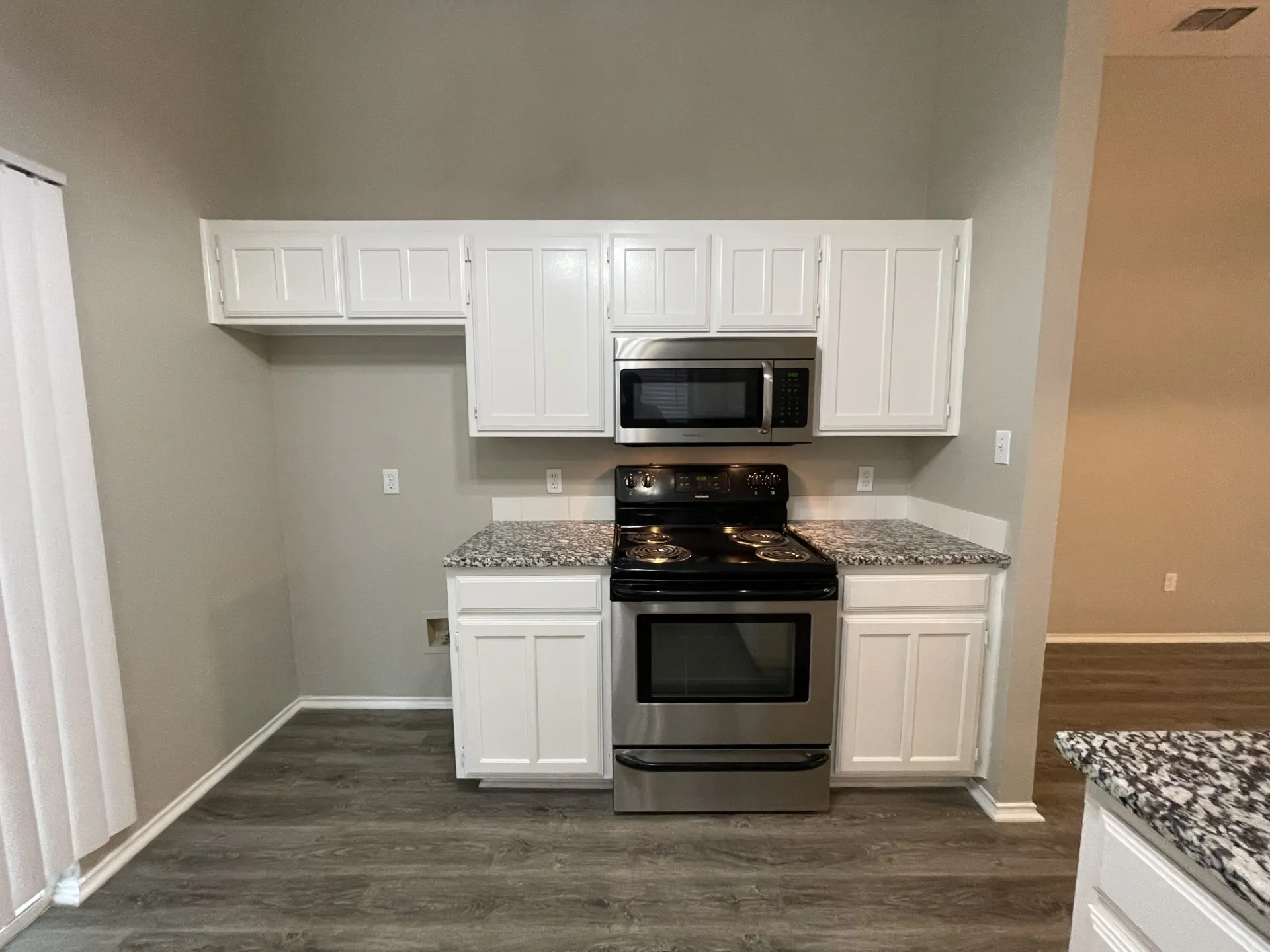 White cabinetry with stainless steel appliances, granite-style countertops, and wood-finish flooring