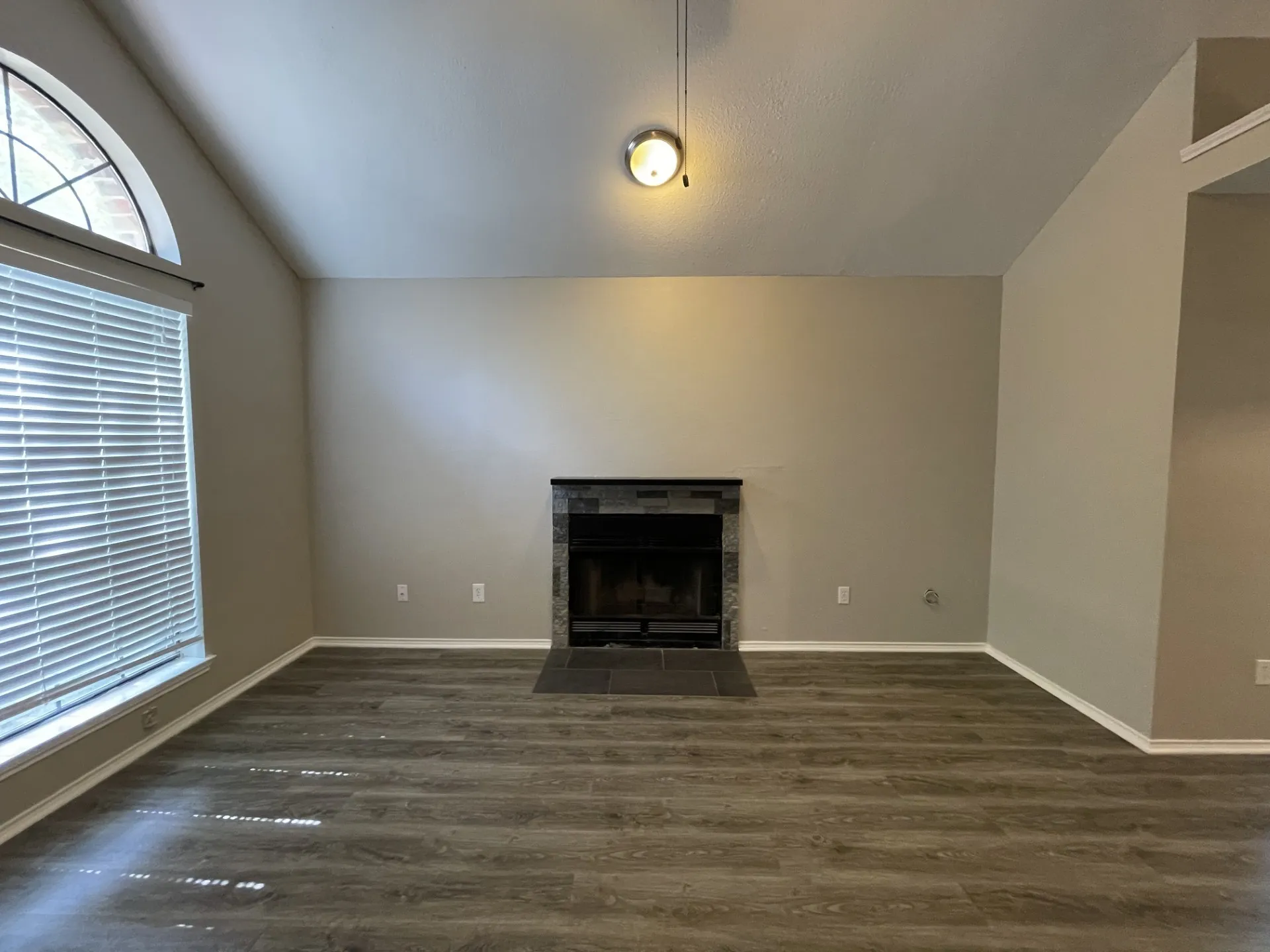 Vaulted ceiling with an arched window, wood-finish flooring, and a fireplace with a stone-tile surround