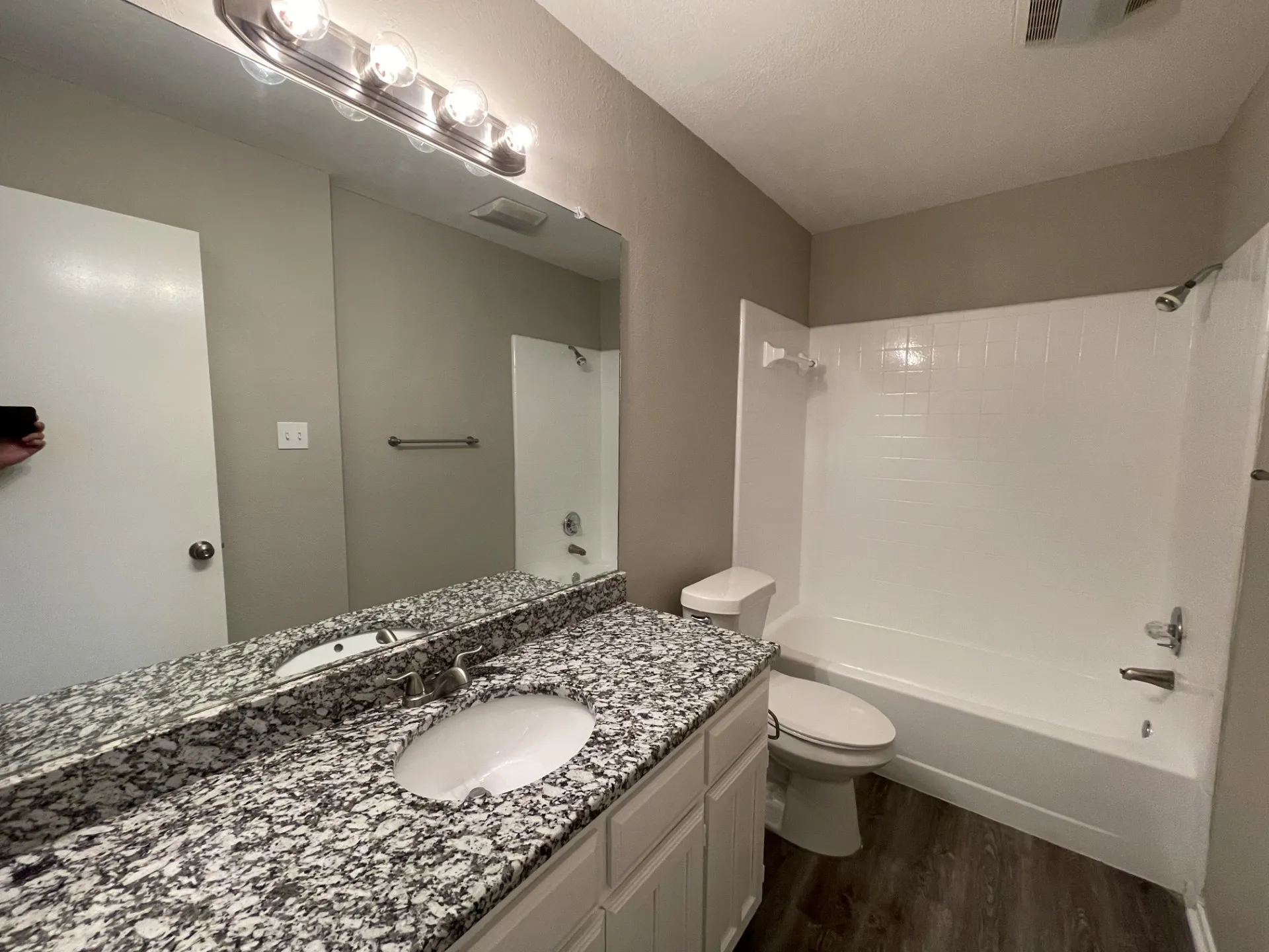 Vanity with stone-finish countertop and undermount sink, full-width mirror, white paneled cabinetry, and wood-finish flooring