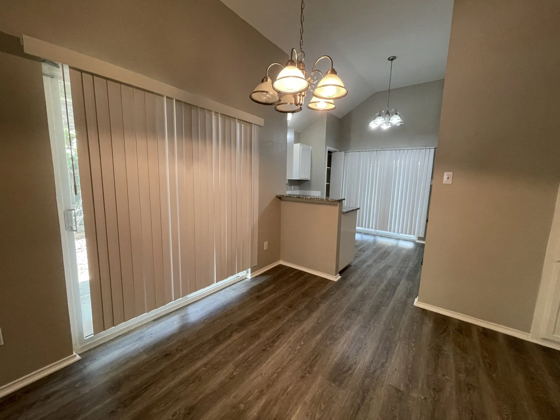 Wood-finish flooring, vaulted ceiling, built-in breakfast bar with stone-look countertop, and sliding glass door with vertical blinds