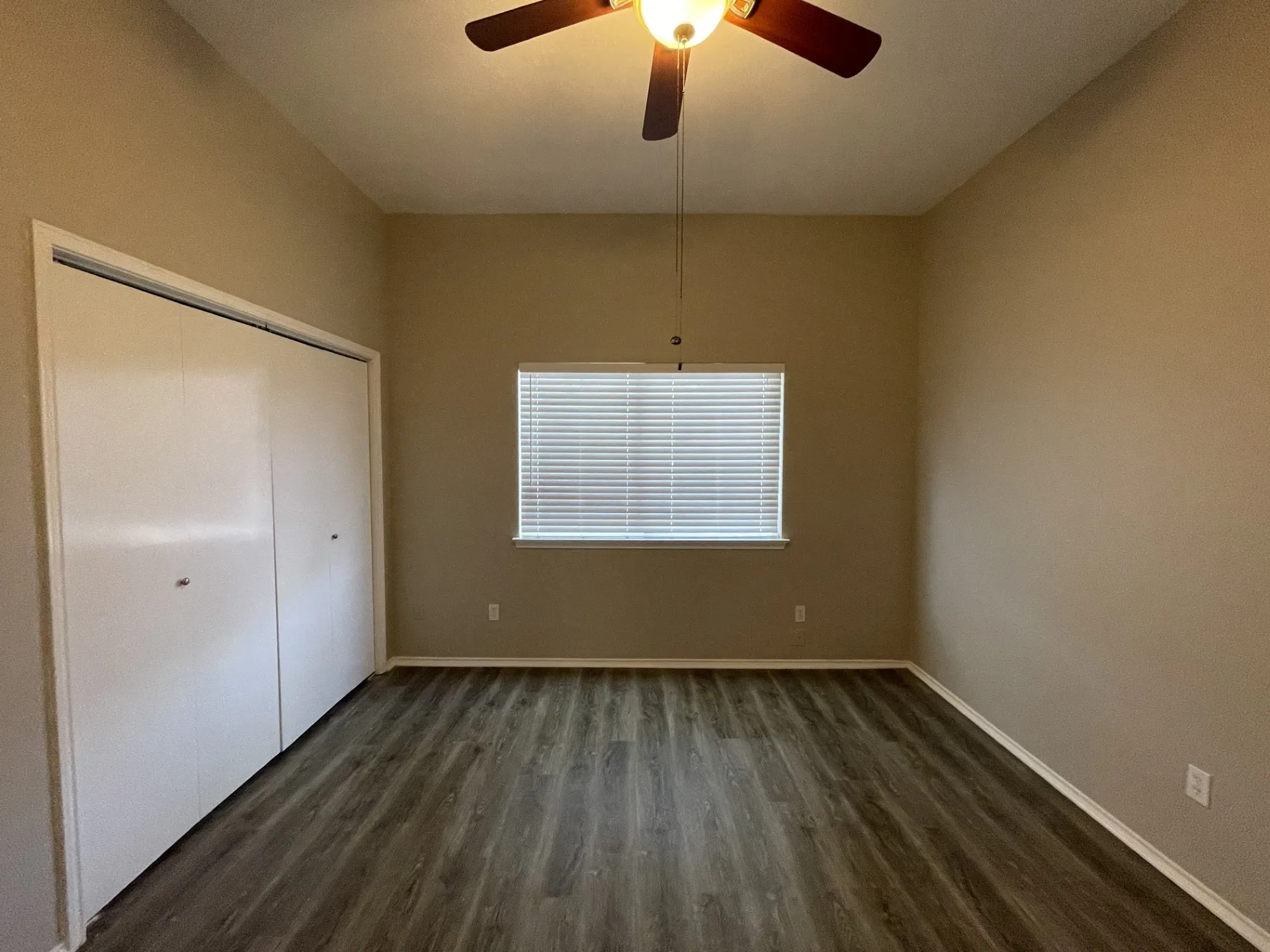 Wood-finish flooring with a neutral wall palette, a built-in closet with bi-fold doors, a window with horizontal blinds, and a ceiling fan with integrated lighting