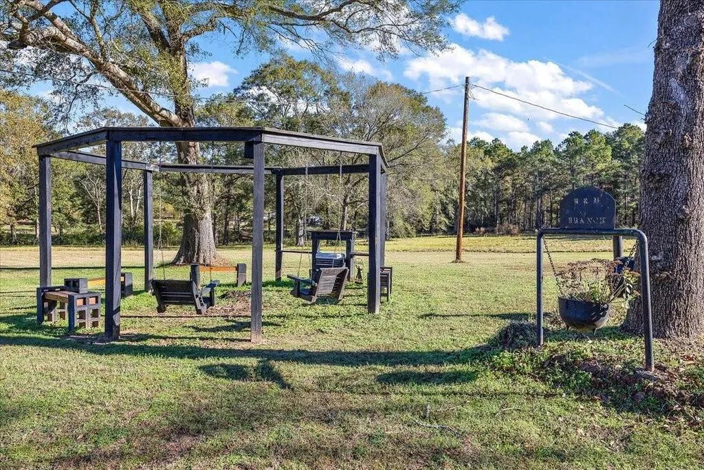 Outdoor wooden swing set structure set amidst tree-shaded lawn grounds.
