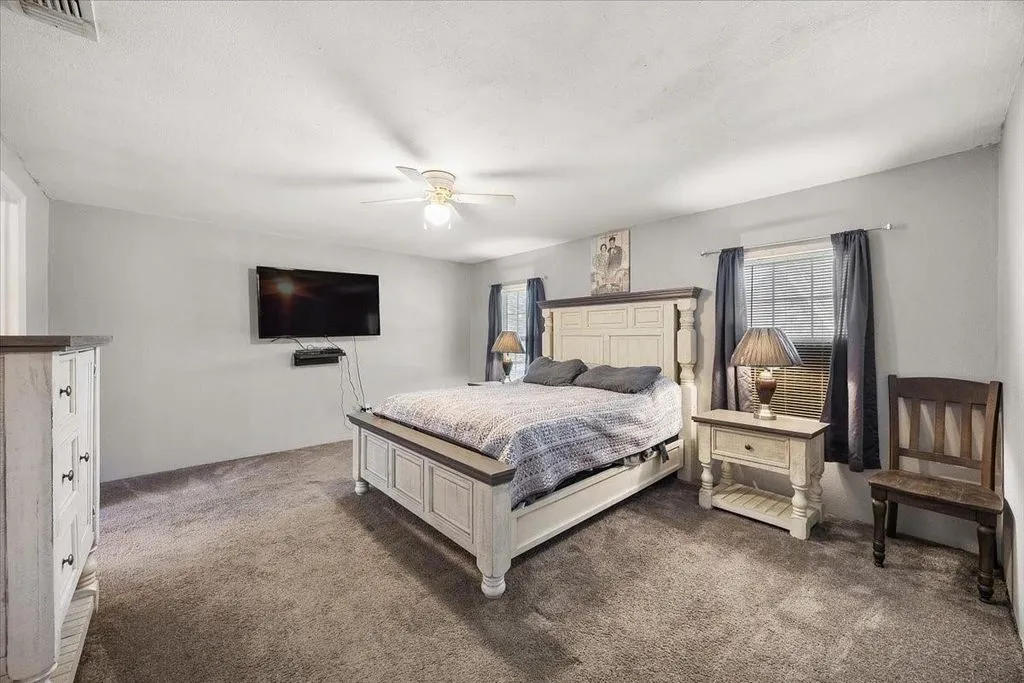 Primary bedroom suite displaying broad layout, carpeted flooring, neutral decor, and ceiling fan.