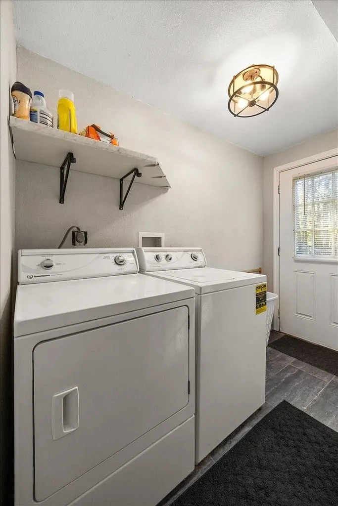 Dedicated laundry utility room fitted with washer, dryer, upper shelving space, and decorative light fixture.