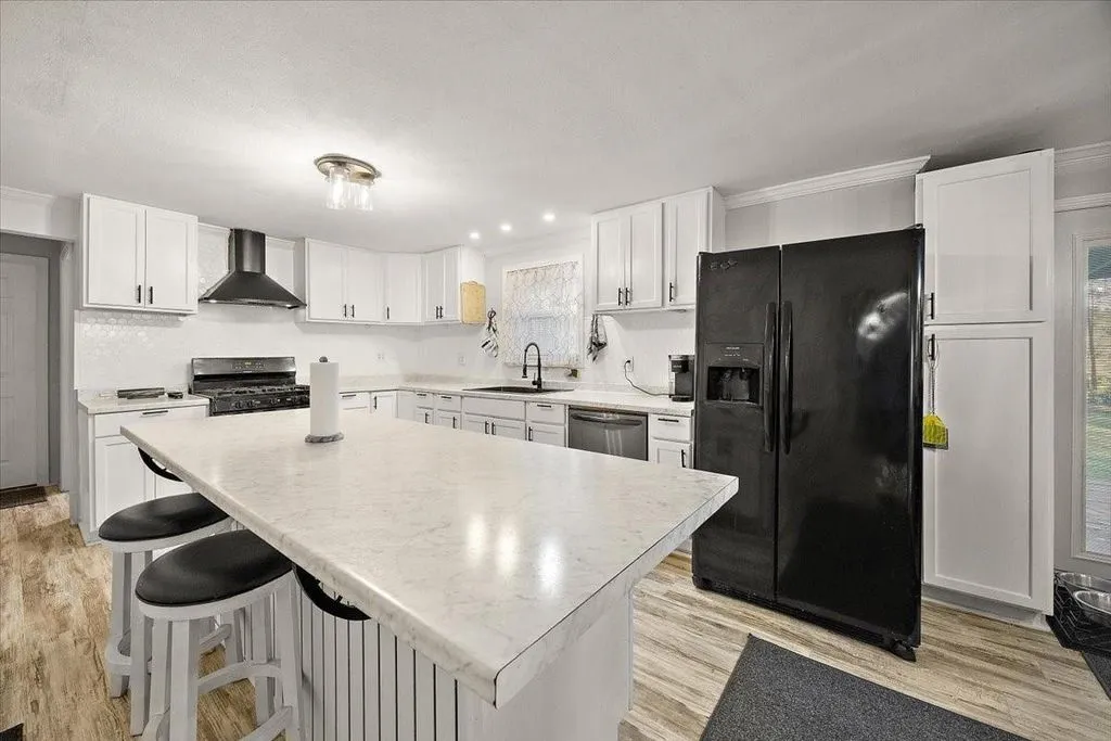 Modern kitchen featuring white shaker cabinetry, central island with seating, black hardware, and dark countertop accents.