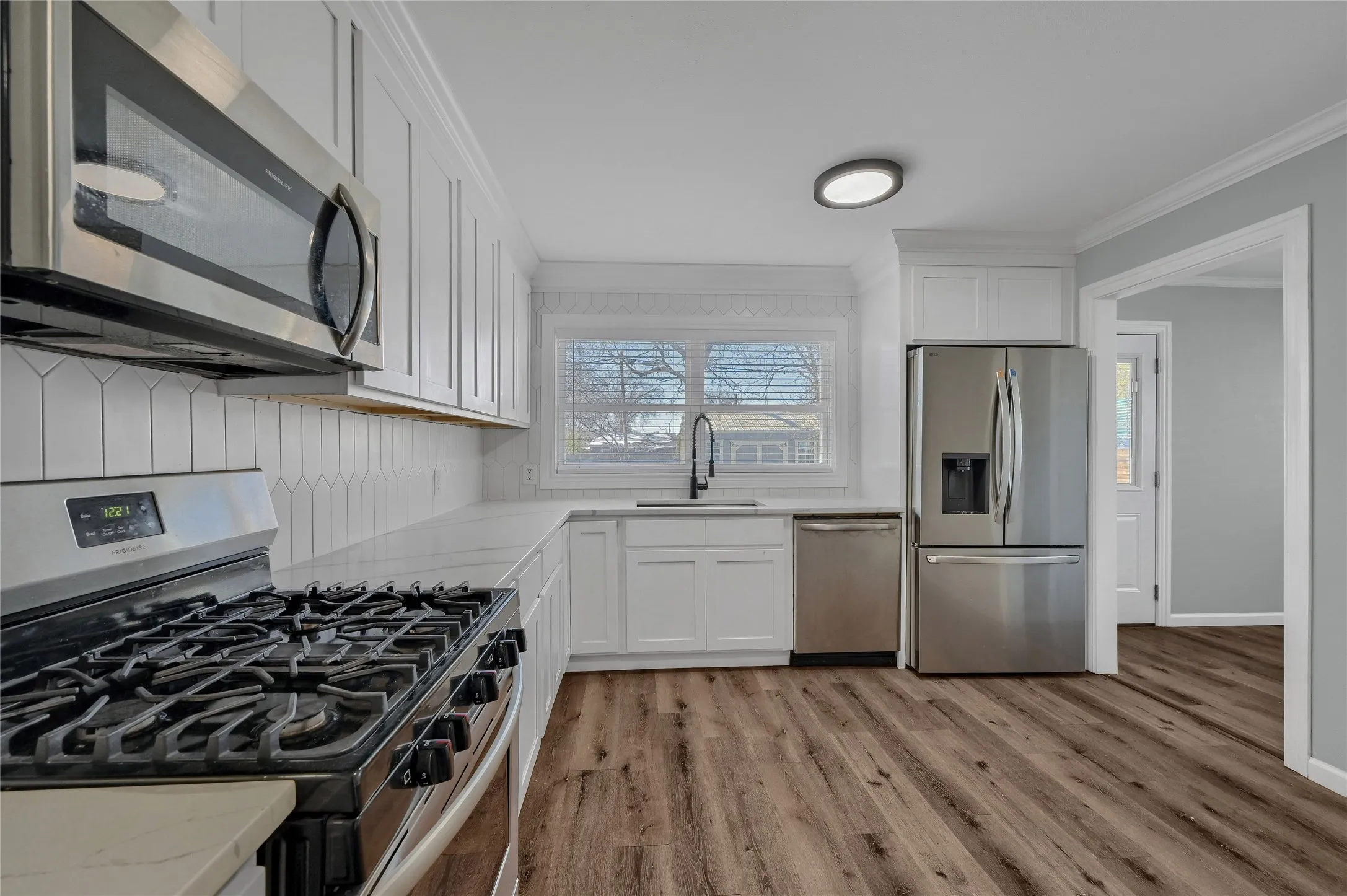 Kitchen with stainless steel appliances, light stone countertops, crown molding, white cabinets, and sink
