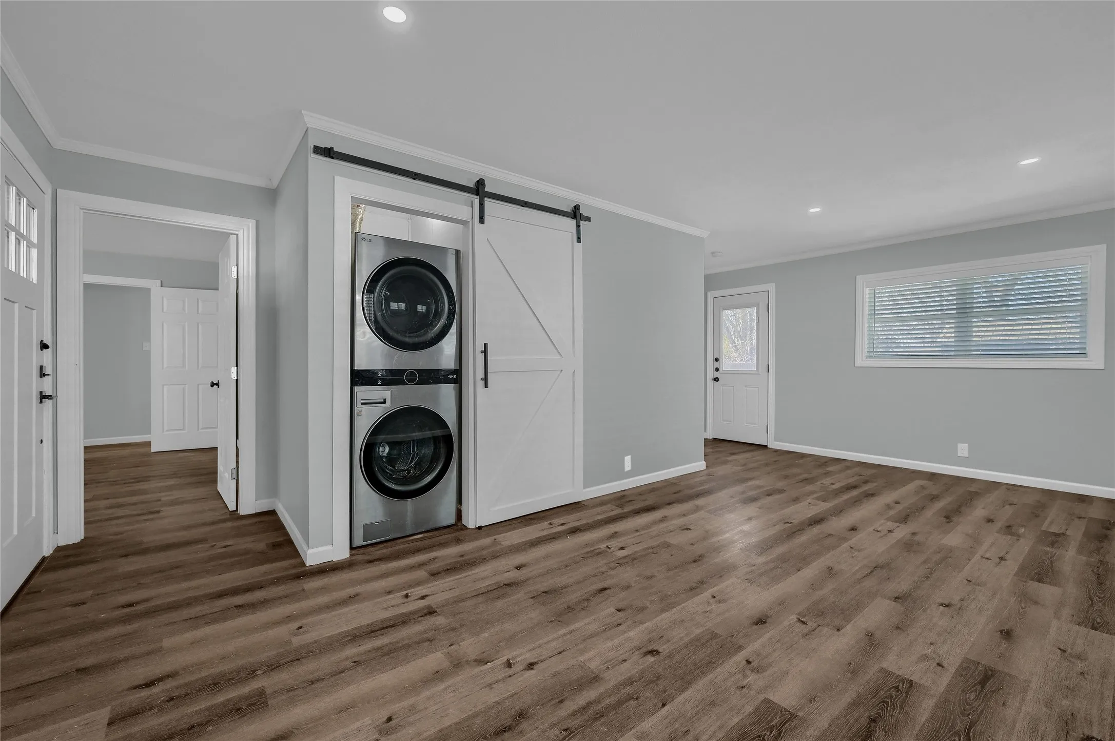 Clothes washing area featuring wood-type flooring, crown molding, stacked washer and dryer, and a barn door