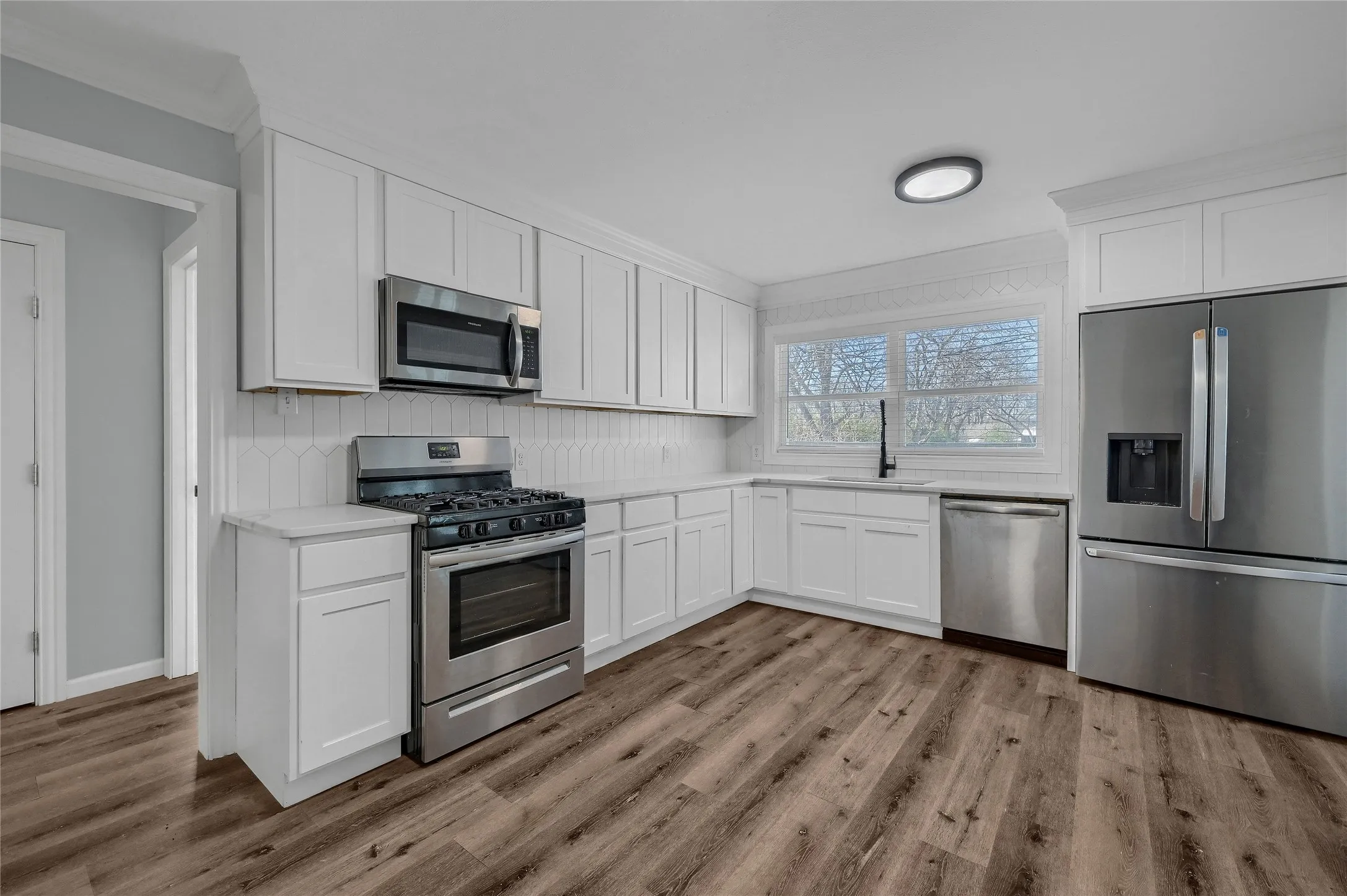 Kitchen featuring appliances with stainless steel finishes, white cabinetry, decorative backsplash, sink, and ornamental molding