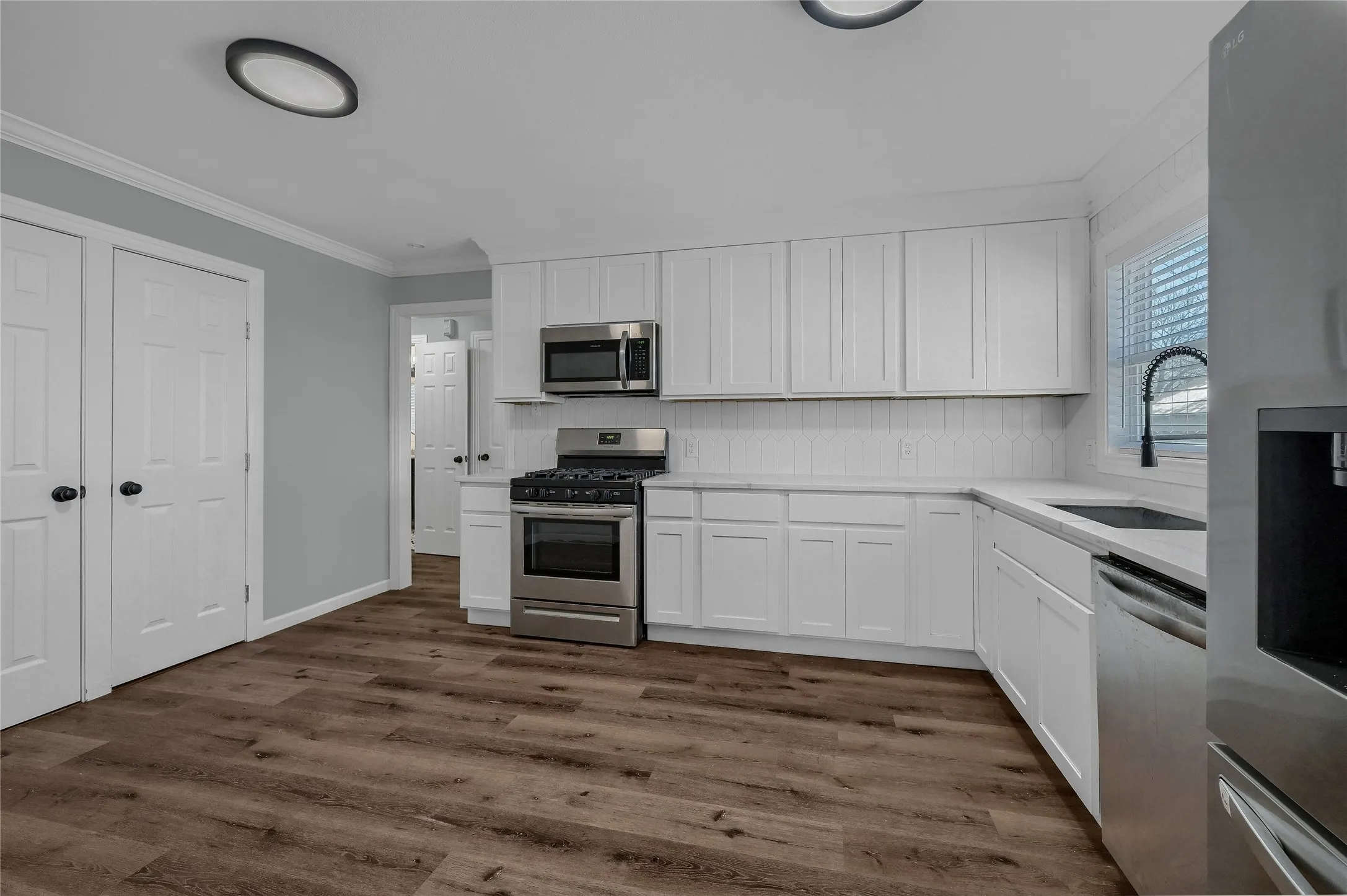 Kitchen with dark wood-type flooring, white cabinetry, stainless steel appliances, sink, and crown molding