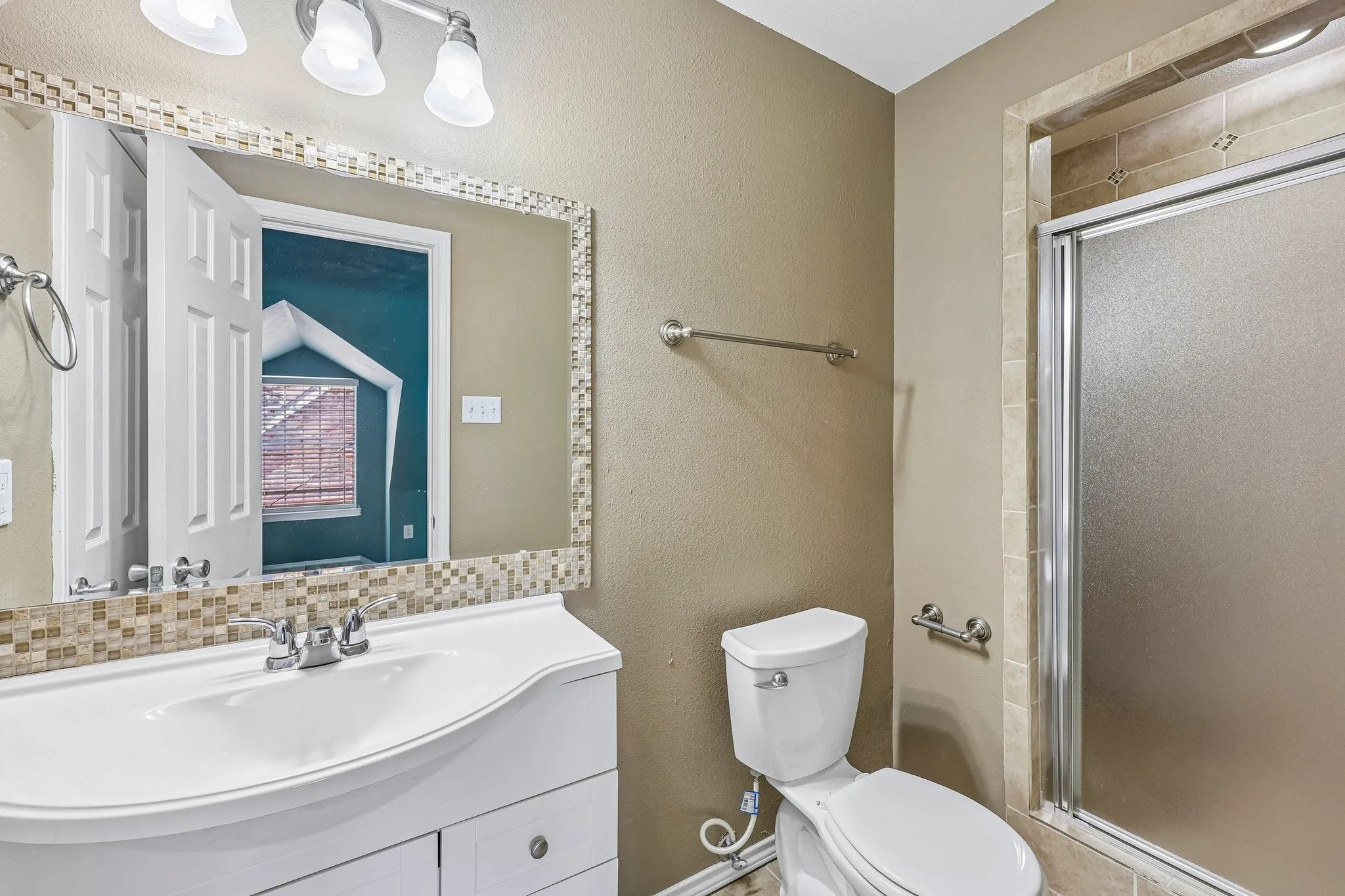 Bathroom featuring a white vanity with integrated sink, chrome faucet, and a mirror framed with mosaic tiles