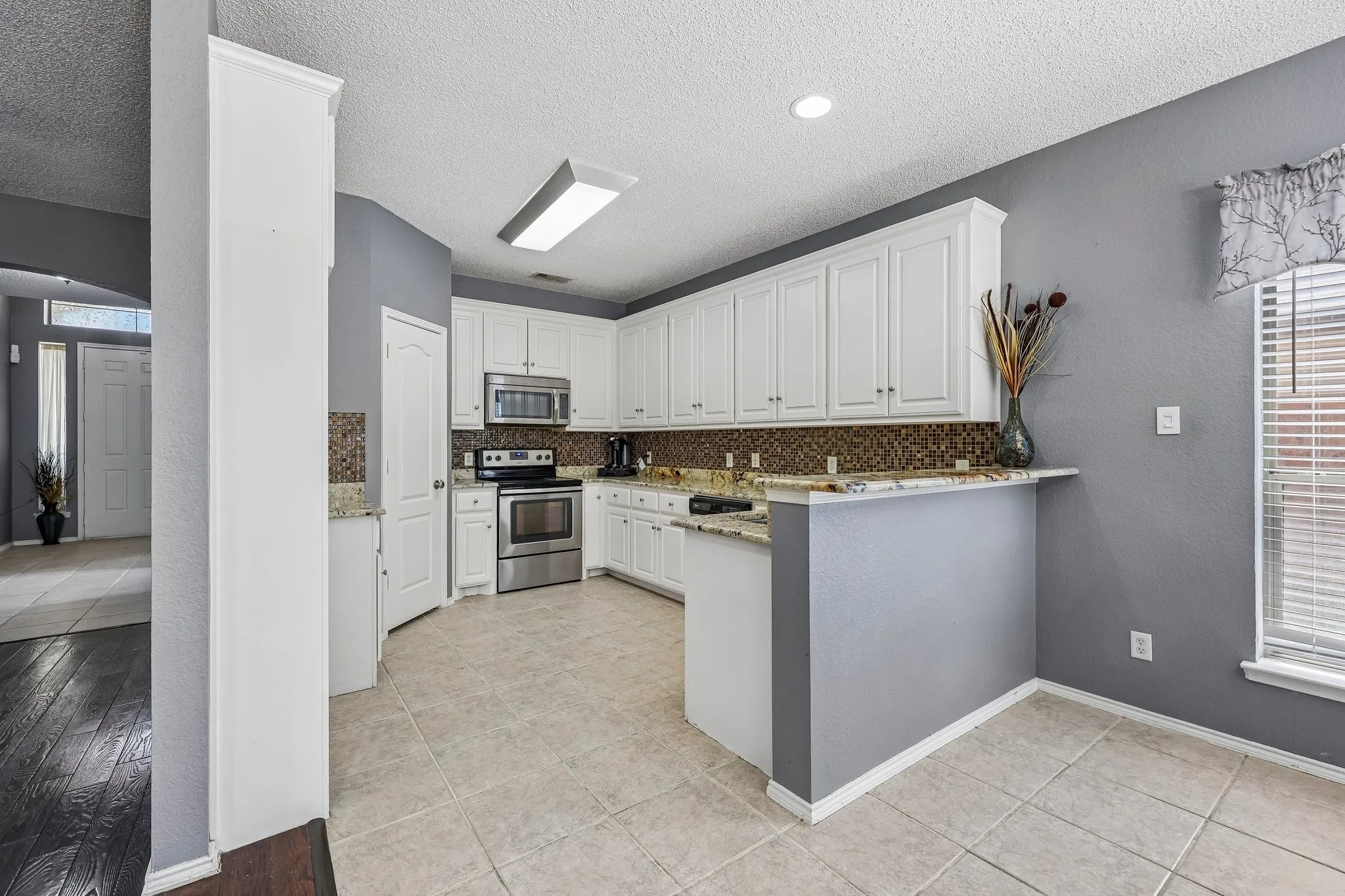 Kitchen featuring white cabinetry, stainless steel appliances, mosaic tile backsplash, and light-toned tile flooring