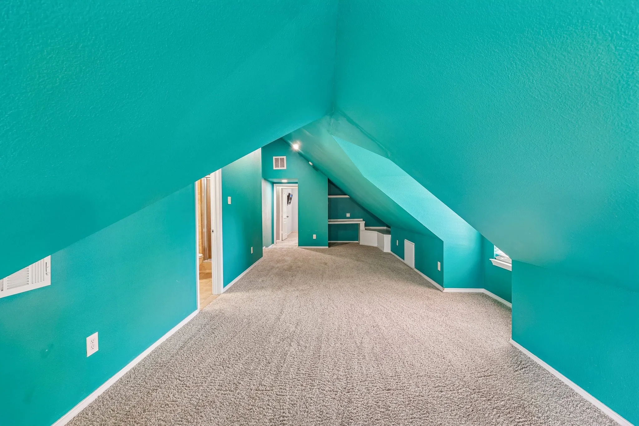 Expansive carpeted room with sloped ceilings and vibrant turquoise walls