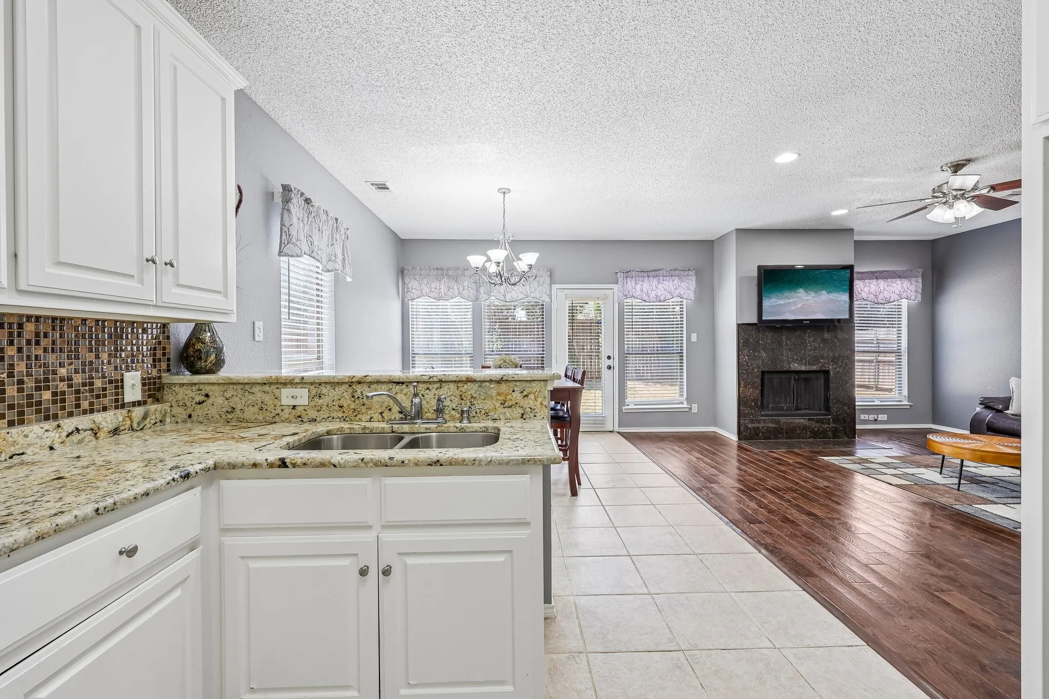 Kitchen featuring white cabinetry, a double basin stainless steel sink, and granite countertops with a mosaic tile backsplash