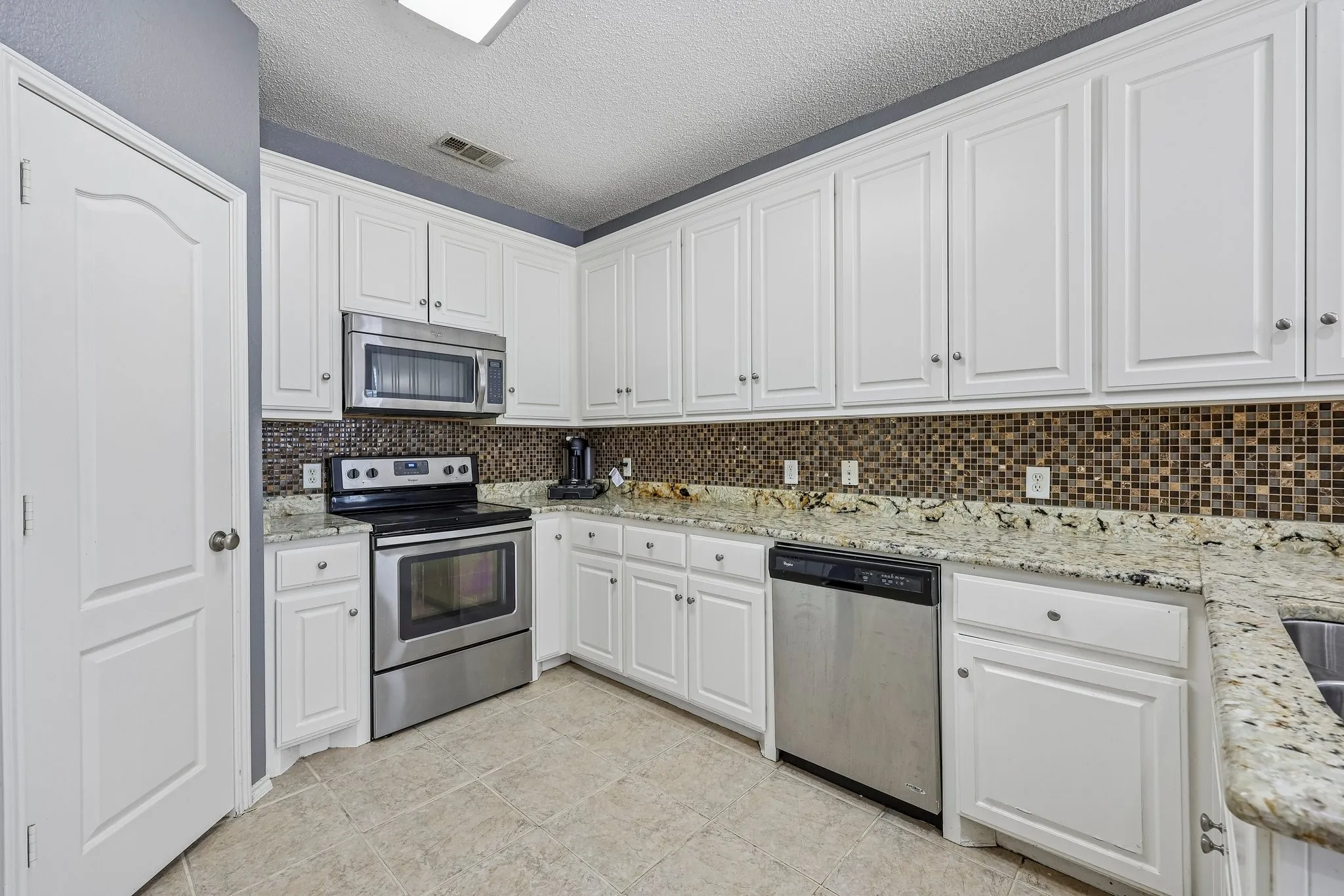 Kitchen featuring white cabinetry, stone countertops, stainless steel appliances, a mosaic tile backsplash, and light-toned tile flooring