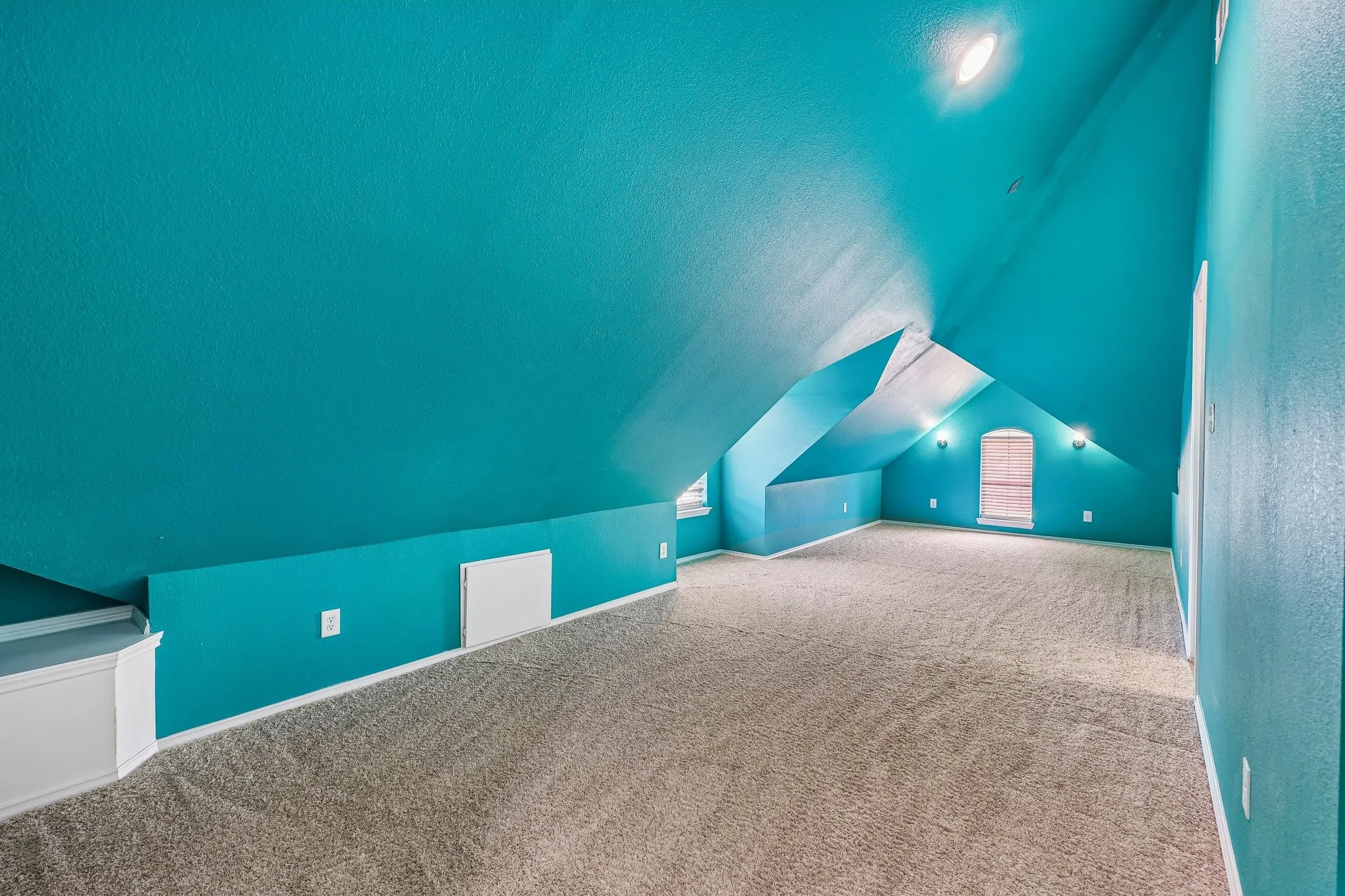Spacious room featuring textured teal walls, sloped ceilings, and light-colored carpeting