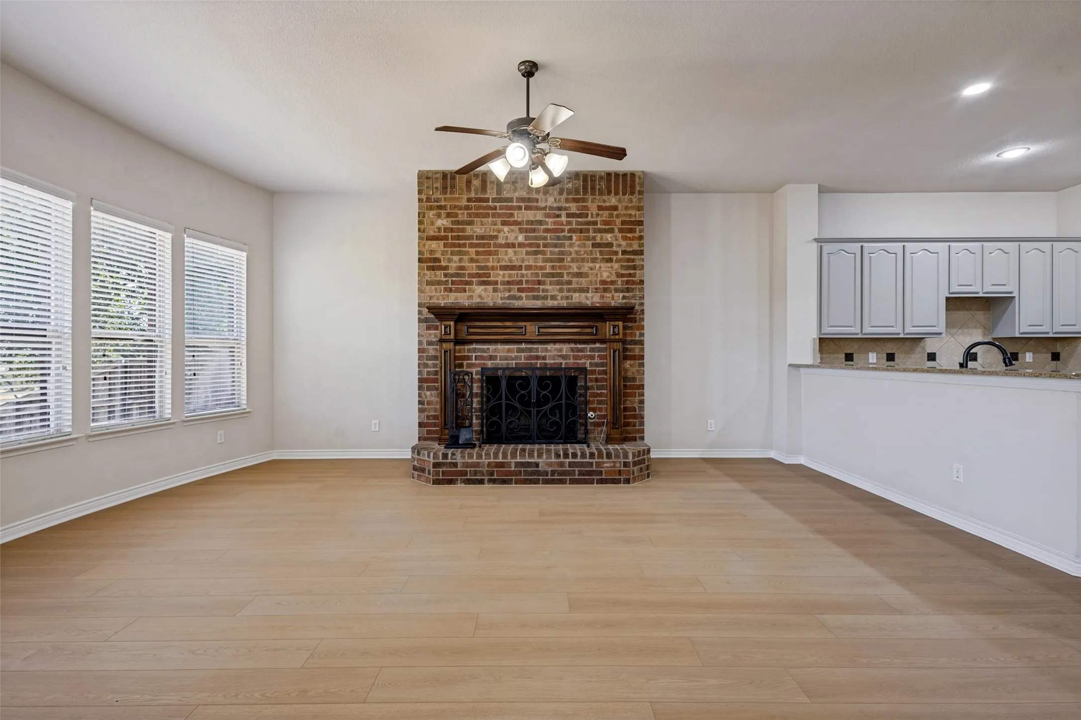 Spacious room featuring wood-finish flooring, a brick fireplace with a wood mantle, and multiple windows with blinds