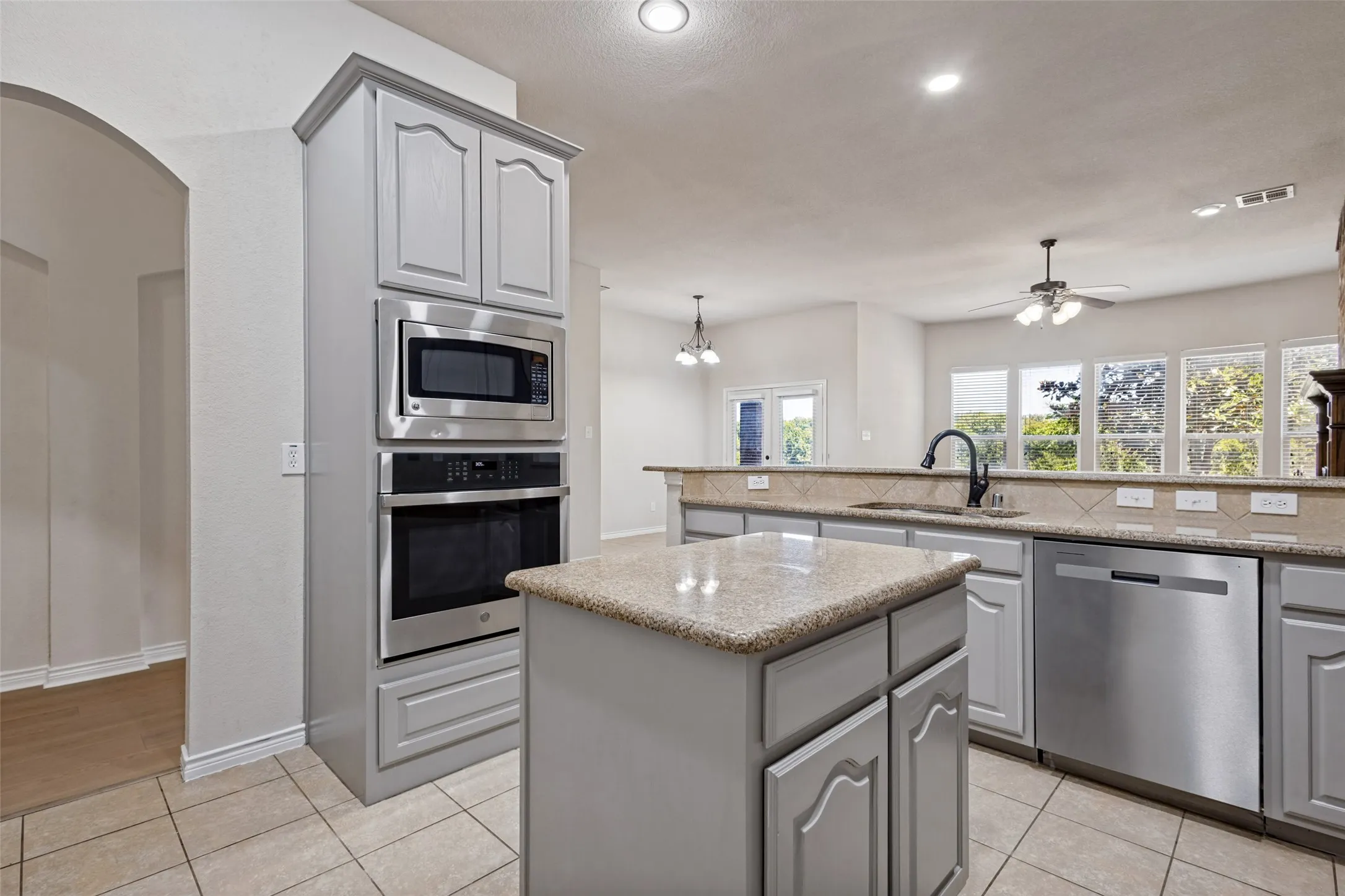 Kitchen featuring gray cabinetry, stainless steel built-in appliances, a central island with a stone countertop, and tile flooring