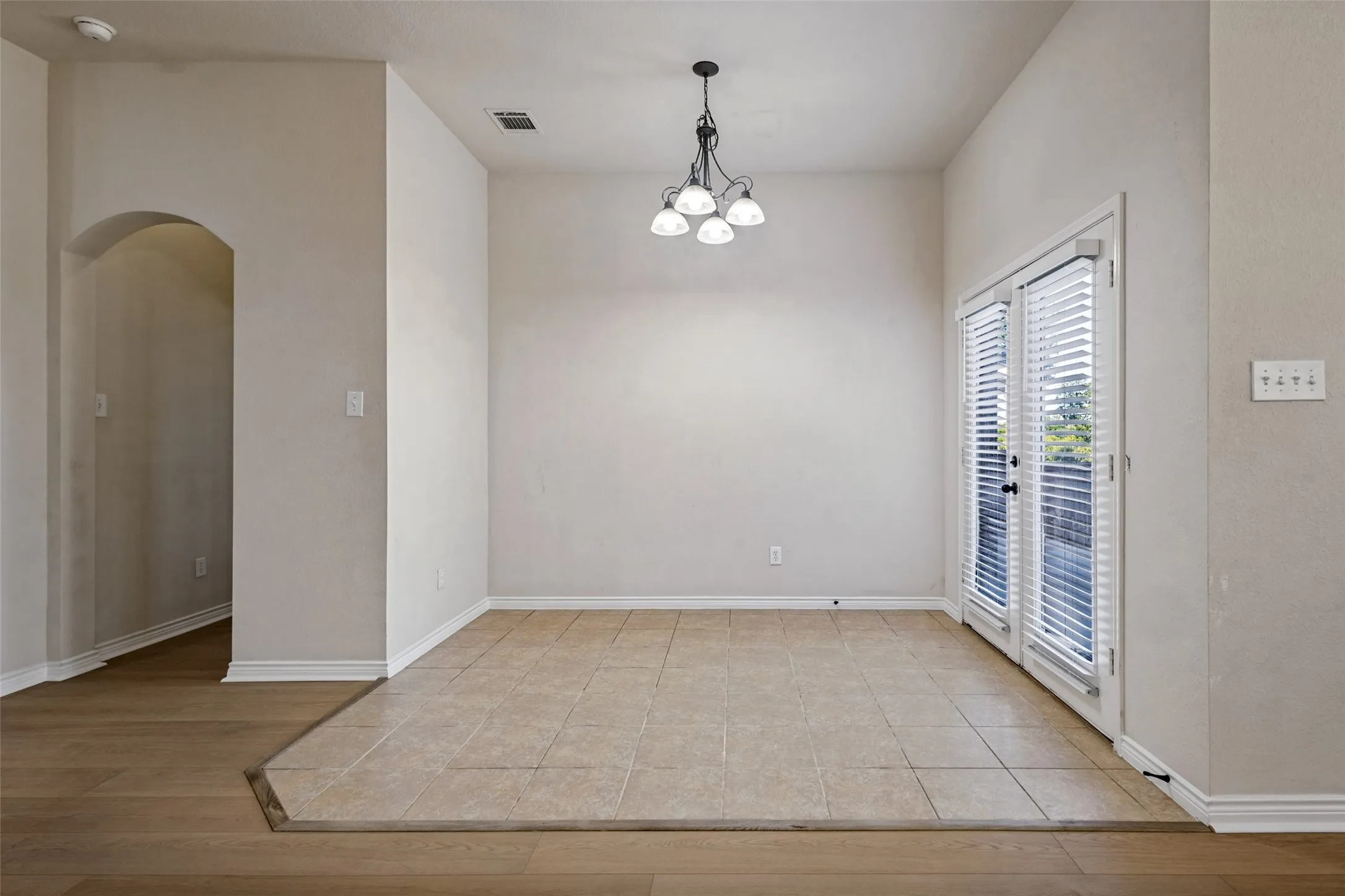 Tile flooring, dual French doors with integrated blinds, wood-finish flooring, archway entrance, and a multi-bulb chandelier