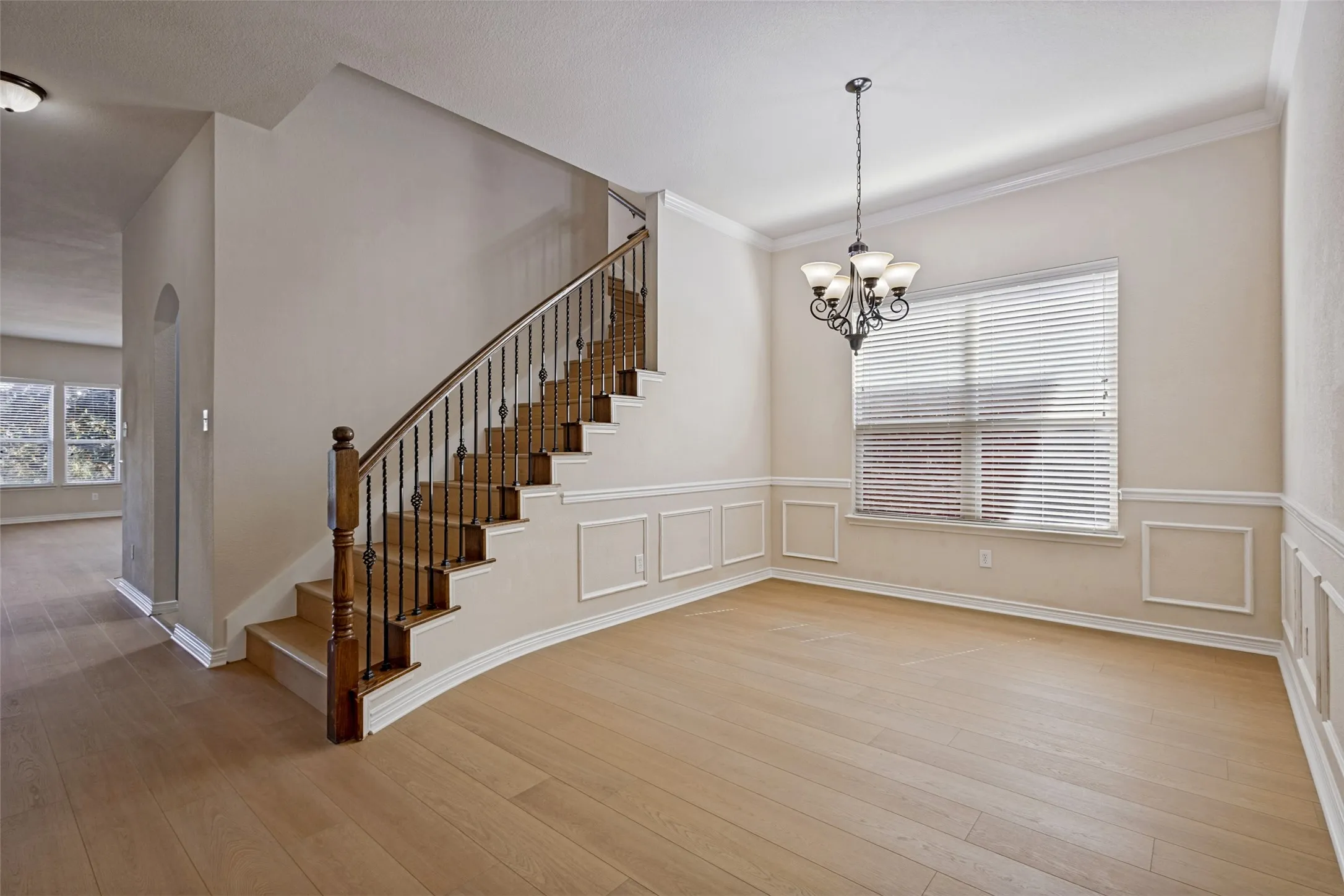 Wood-finish flooring throughout, curved staircase with wrought iron balusters, wainscoting details, crown molding, and a five-light chandelier