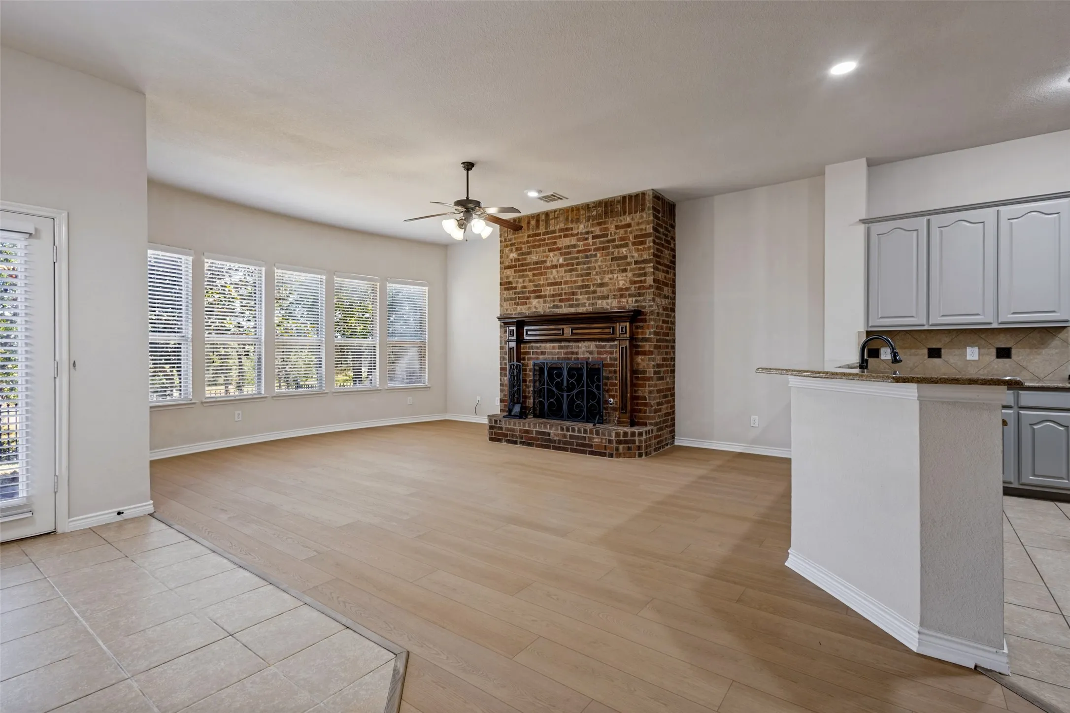 Spacious area featuring a brick fireplace with wood mantel, multiple windows, and a ceiling fan