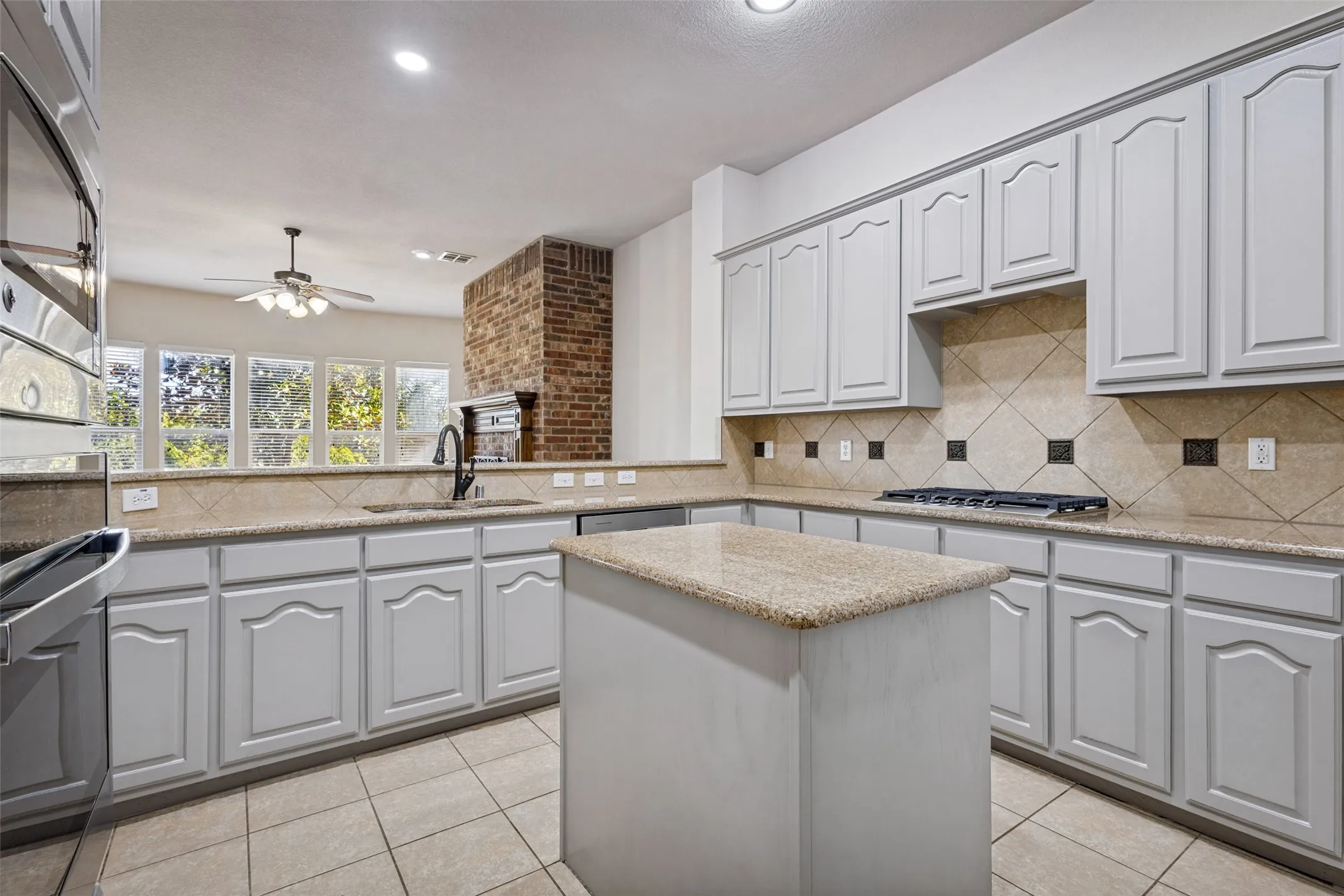 Kitchen featuring light-toned cabinetry, an island with a speckled countertop, a tiled backsplash with accent squares, and a built-in gas cooktop