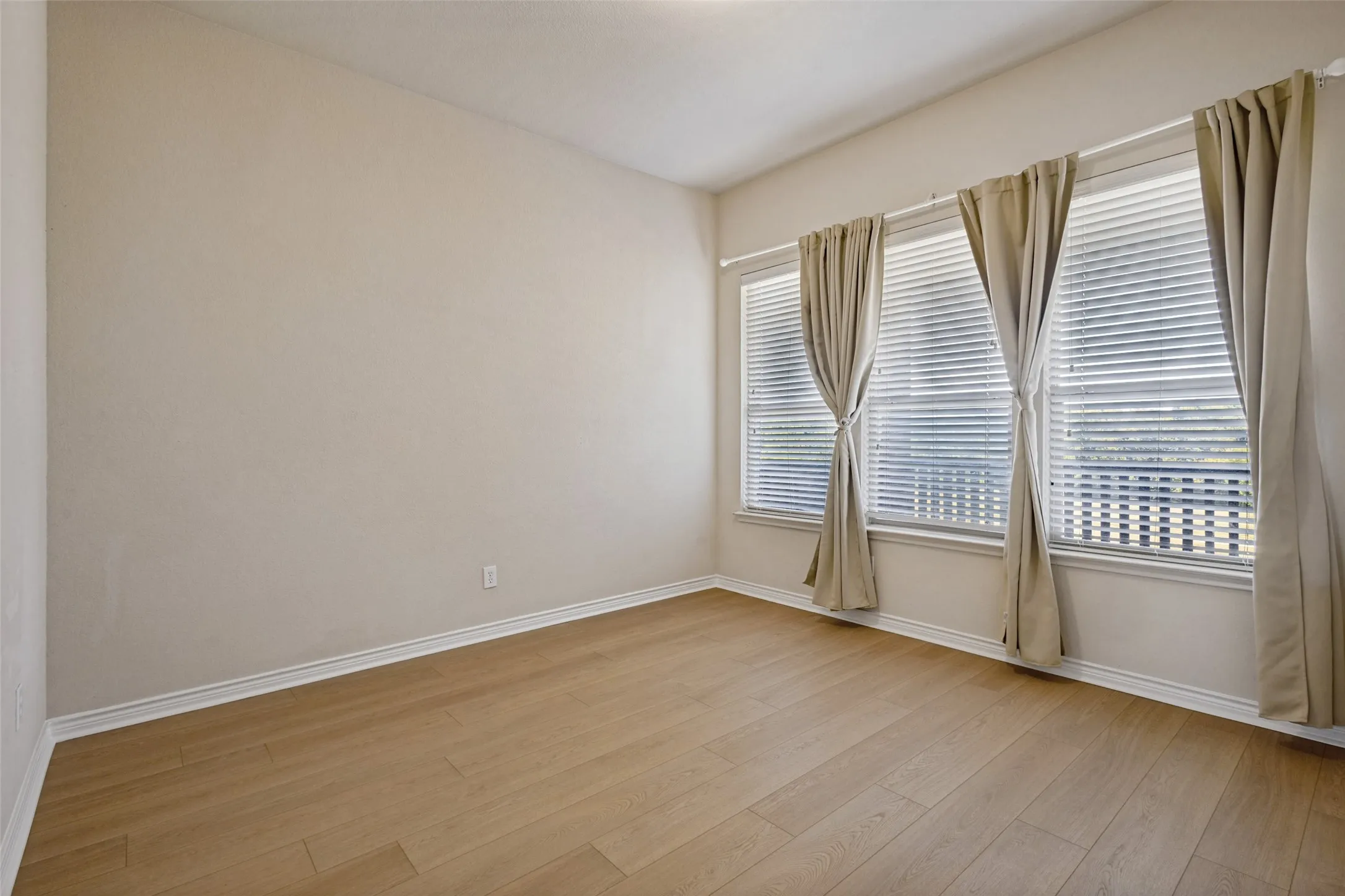 Wood-finish flooring with white trim, featuring three windows with blinds and curtain rods