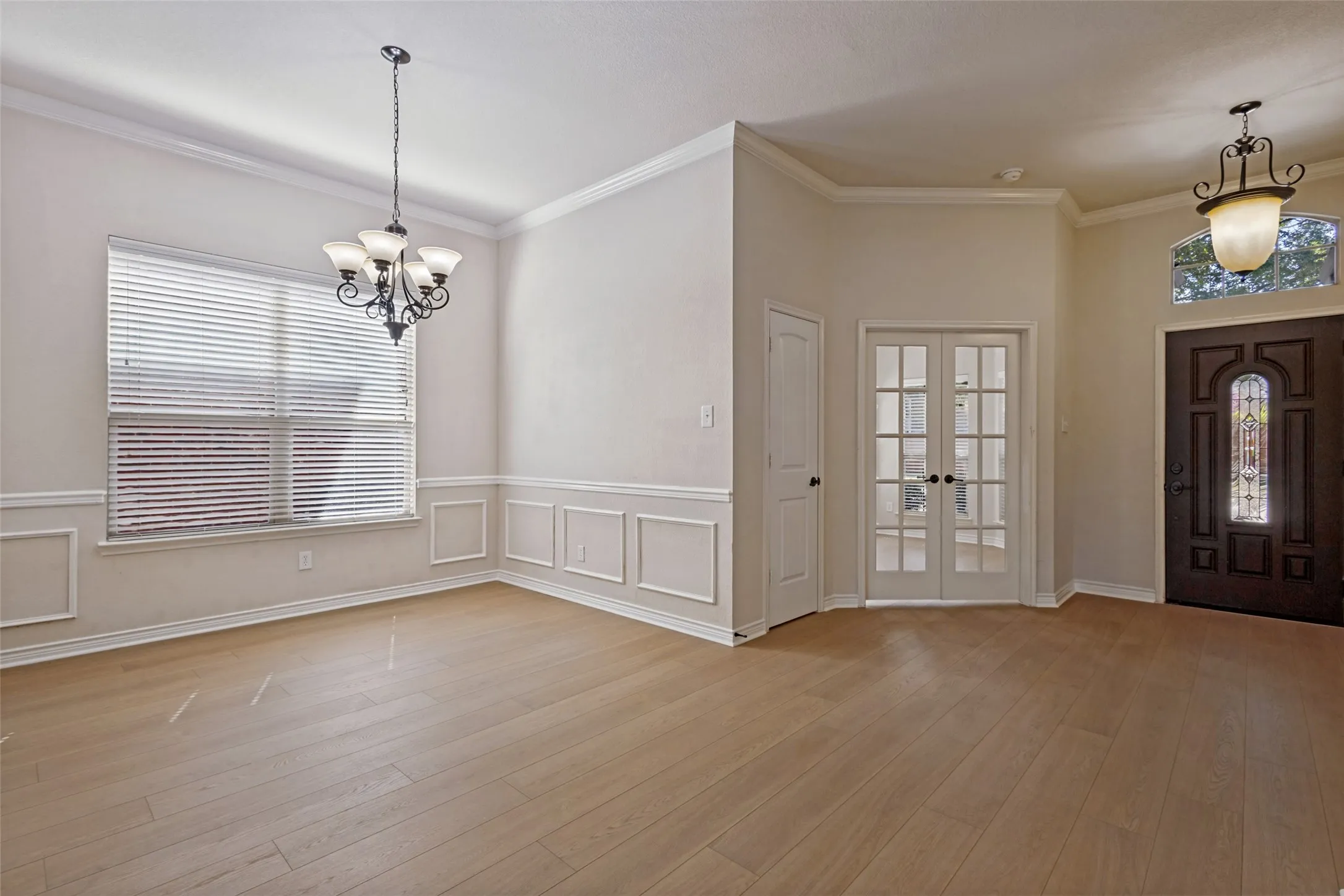 Wood-finish flooring throughout, featuring wainscoting, crown molding, and a decorative chandelier