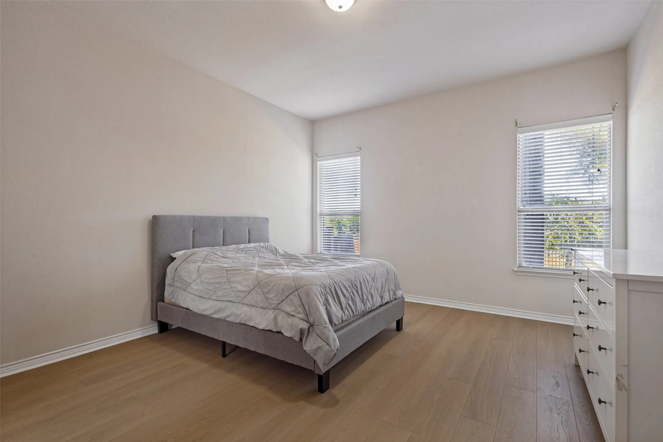Expansive room featuring wood-finish flooring, two windows with blinds, and neutral wall tones