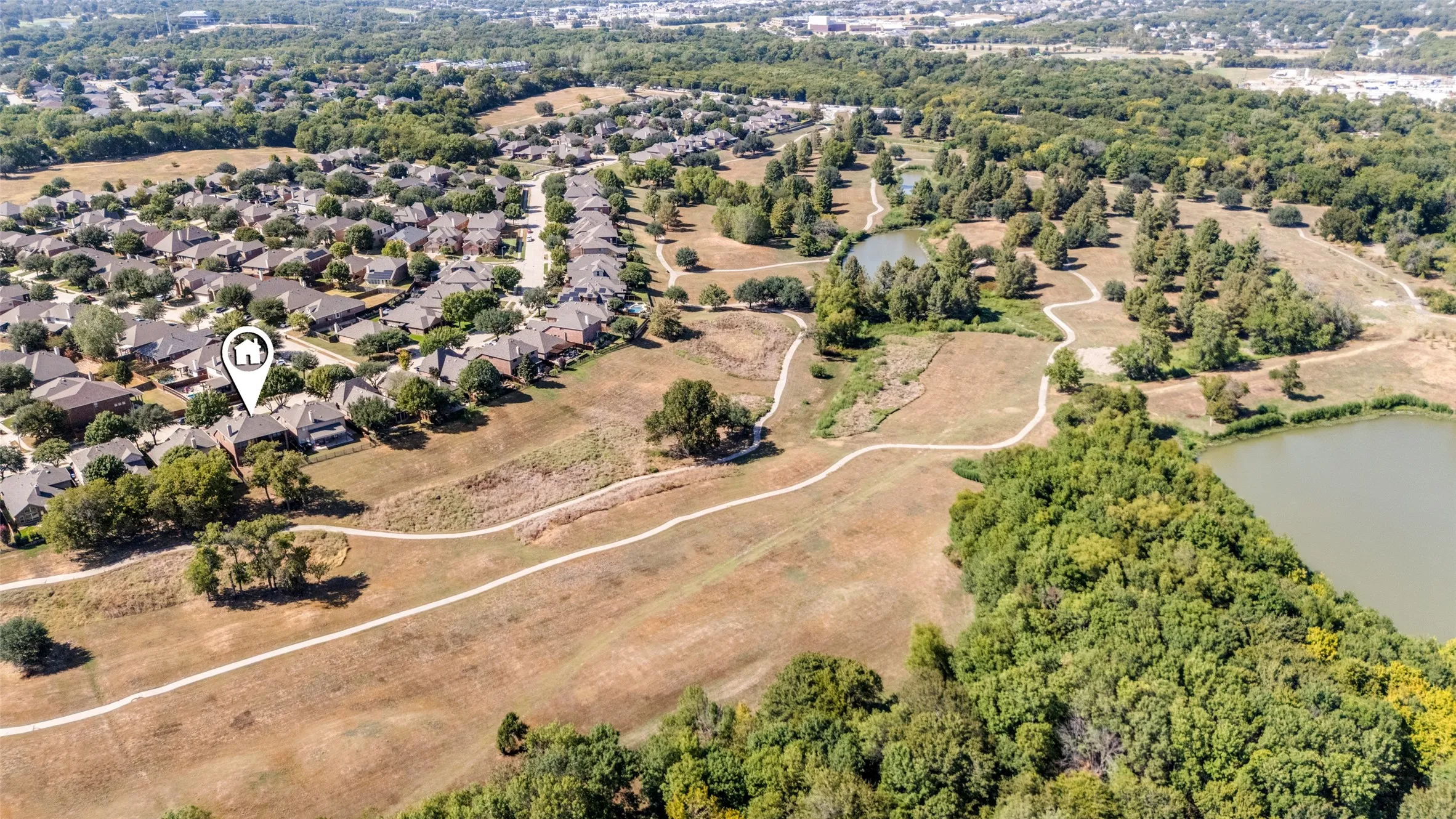 Aerial perspective showcasing a residential neighborhood, expansive green spaces, multiple bodies of water, and surrounding tree coverage