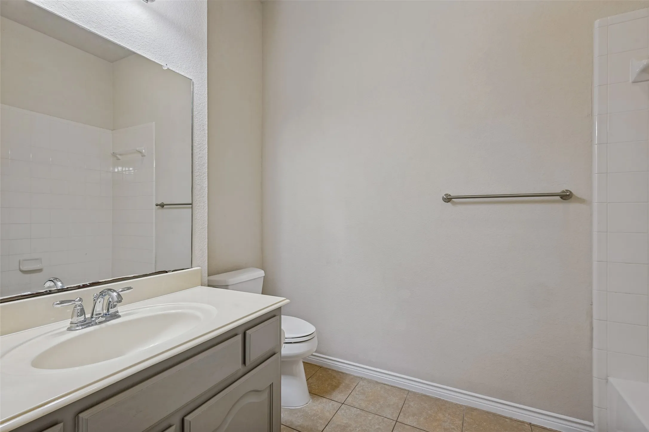 Vanity with an integrated sink and chrome faucet, large wall-mounted mirror, and tiled flooring