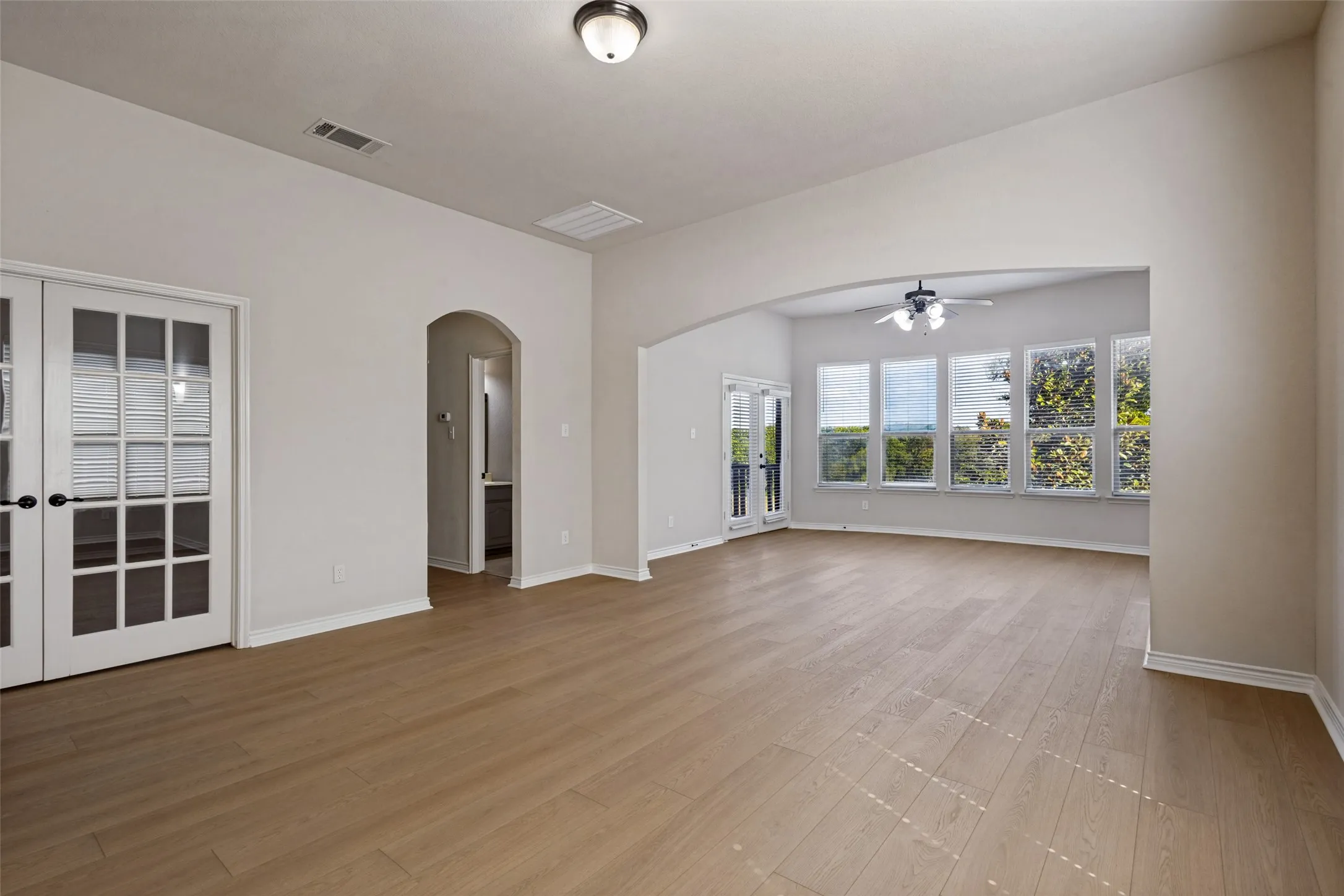 Expansive open-concept room featuring wood-finish flooring, an arched entryway, and multiple large windows