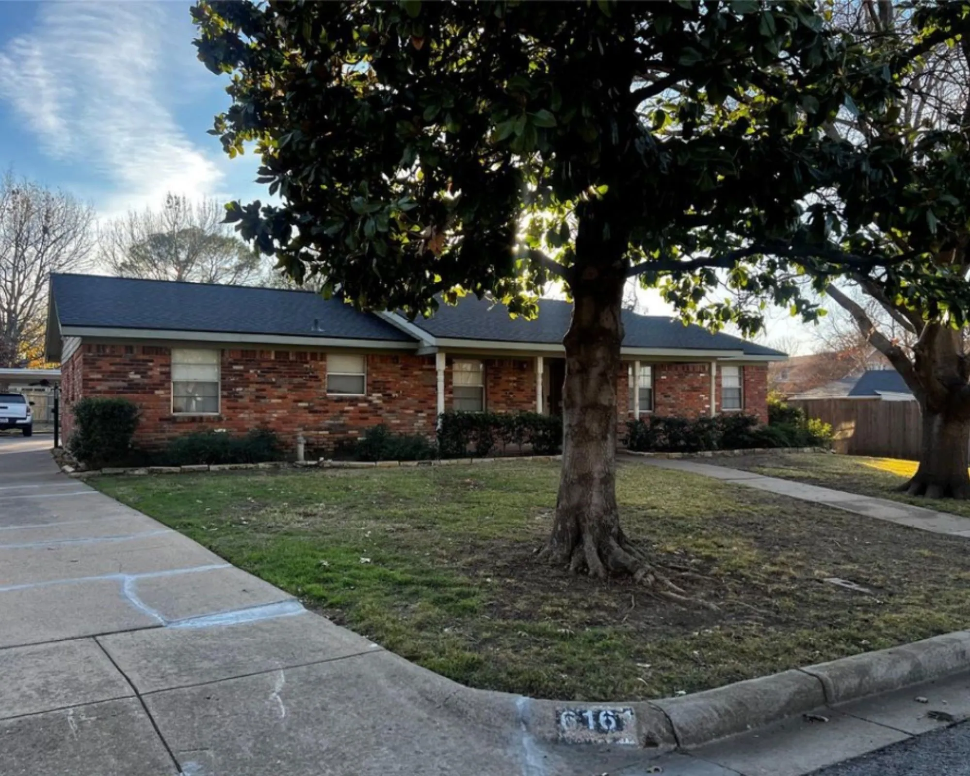 Brick exterior featuring a covered entry and dark shingle roofing