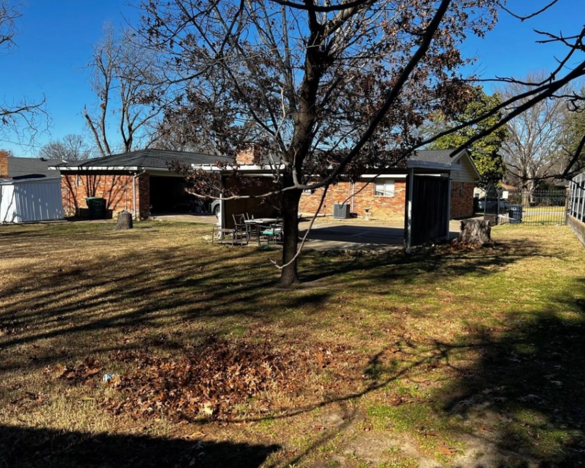 Spacious backyard featuring a brick exterior structure, a covered carport, and mature trees