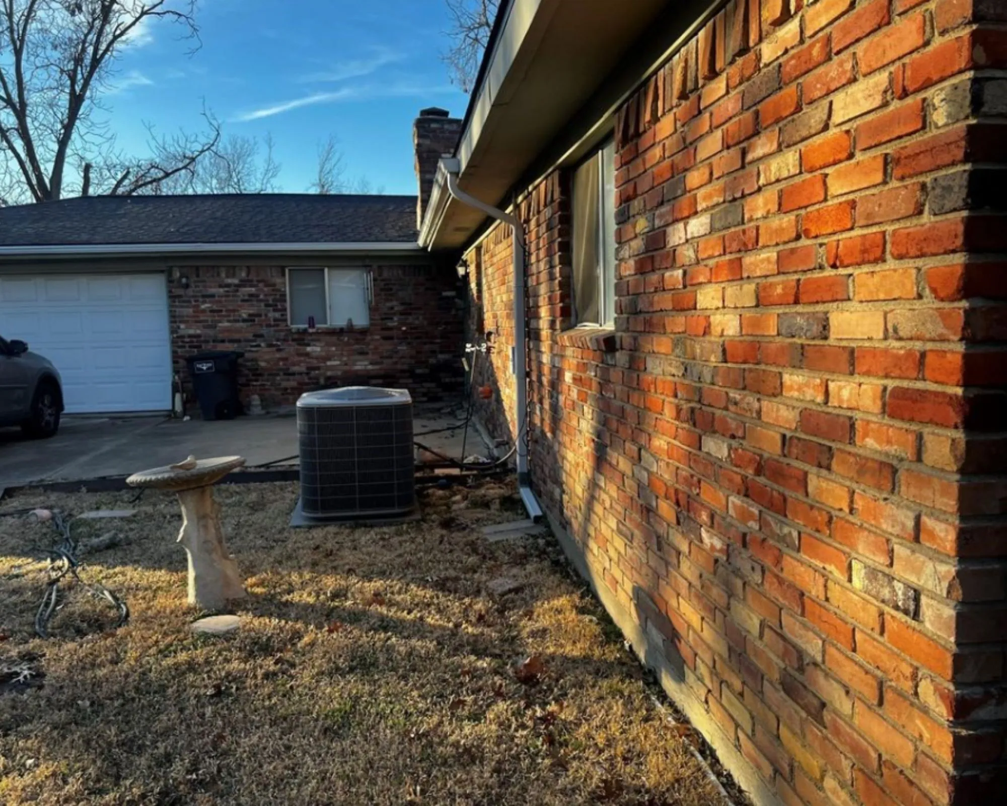 Brick exterior siding with a single-pane window, dark asphalt shingle roof, and attached garage