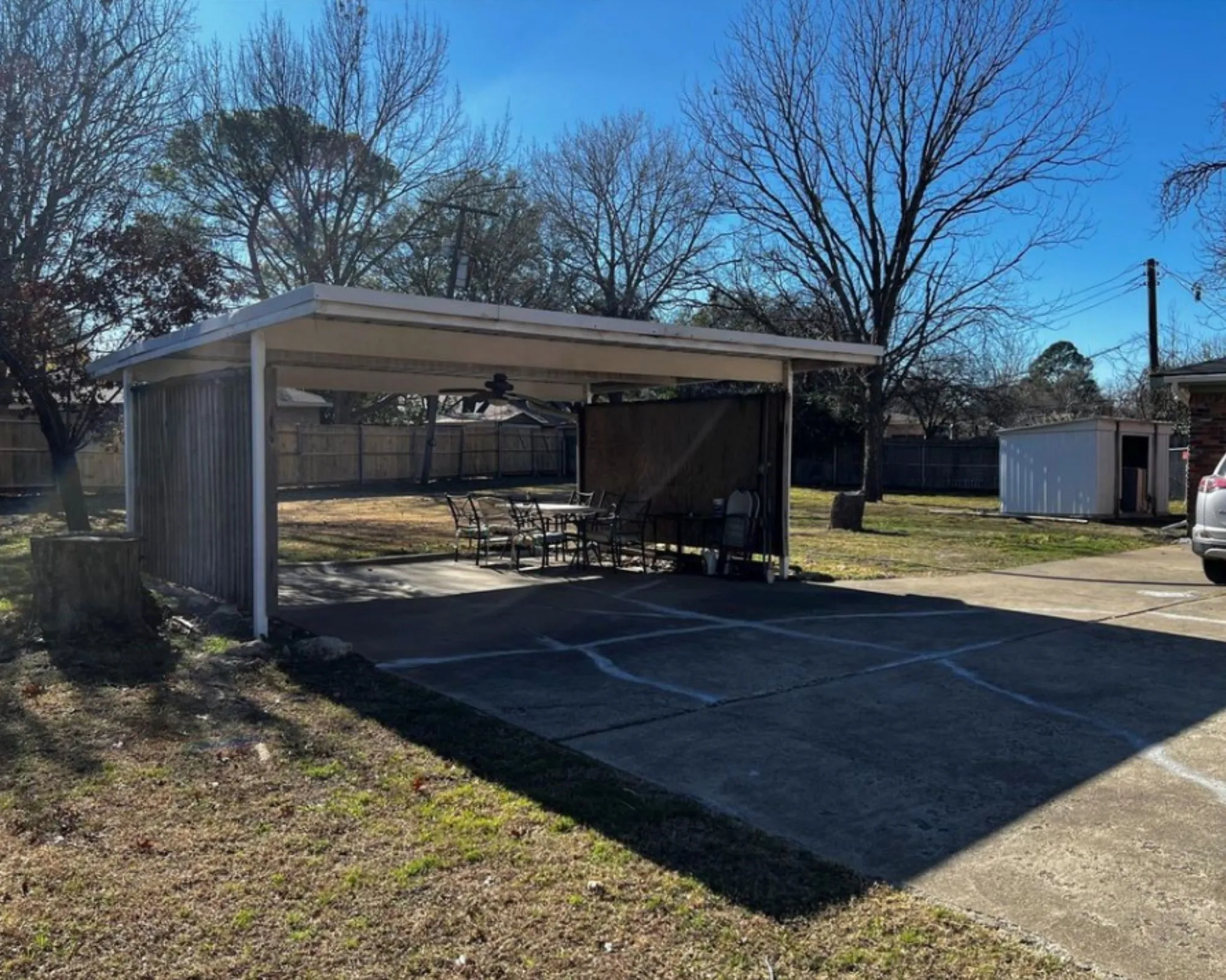 Covered patio area with concrete flooring, wood paneling, and an adjacent concrete driveway