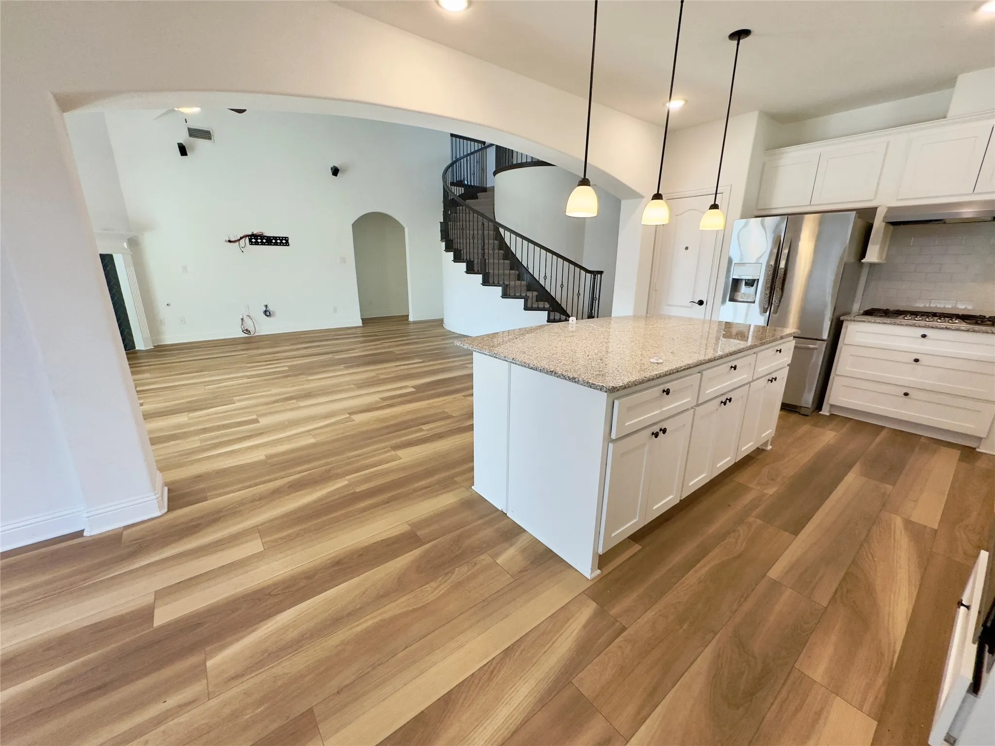 Kitchen with stainless steel appliances, hanging light fixtures, a center island, light stone countertops, and white cabinets
