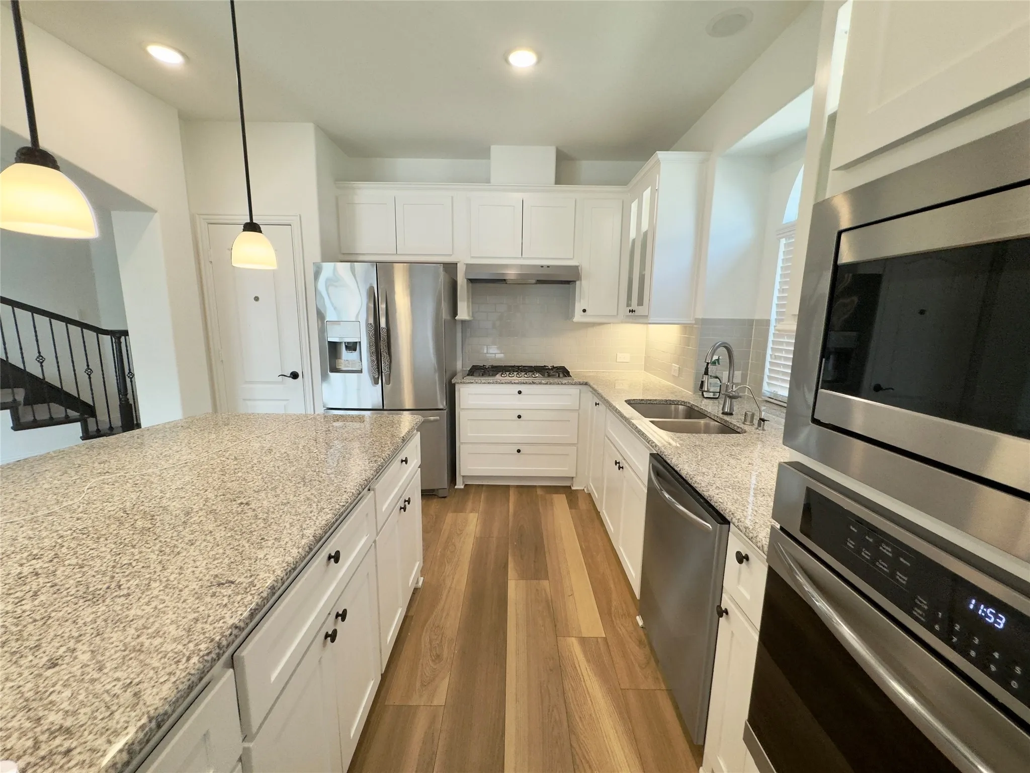 Kitchen featuring stainless steel appliances, sink, white cabinets, backsplash, and hanging light fixtures