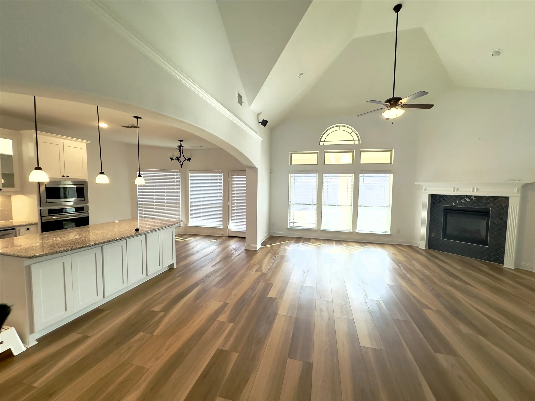Unfurnished living room with ceiling fan with notable chandelier, dark wood-type flooring, and high vaulted ceiling