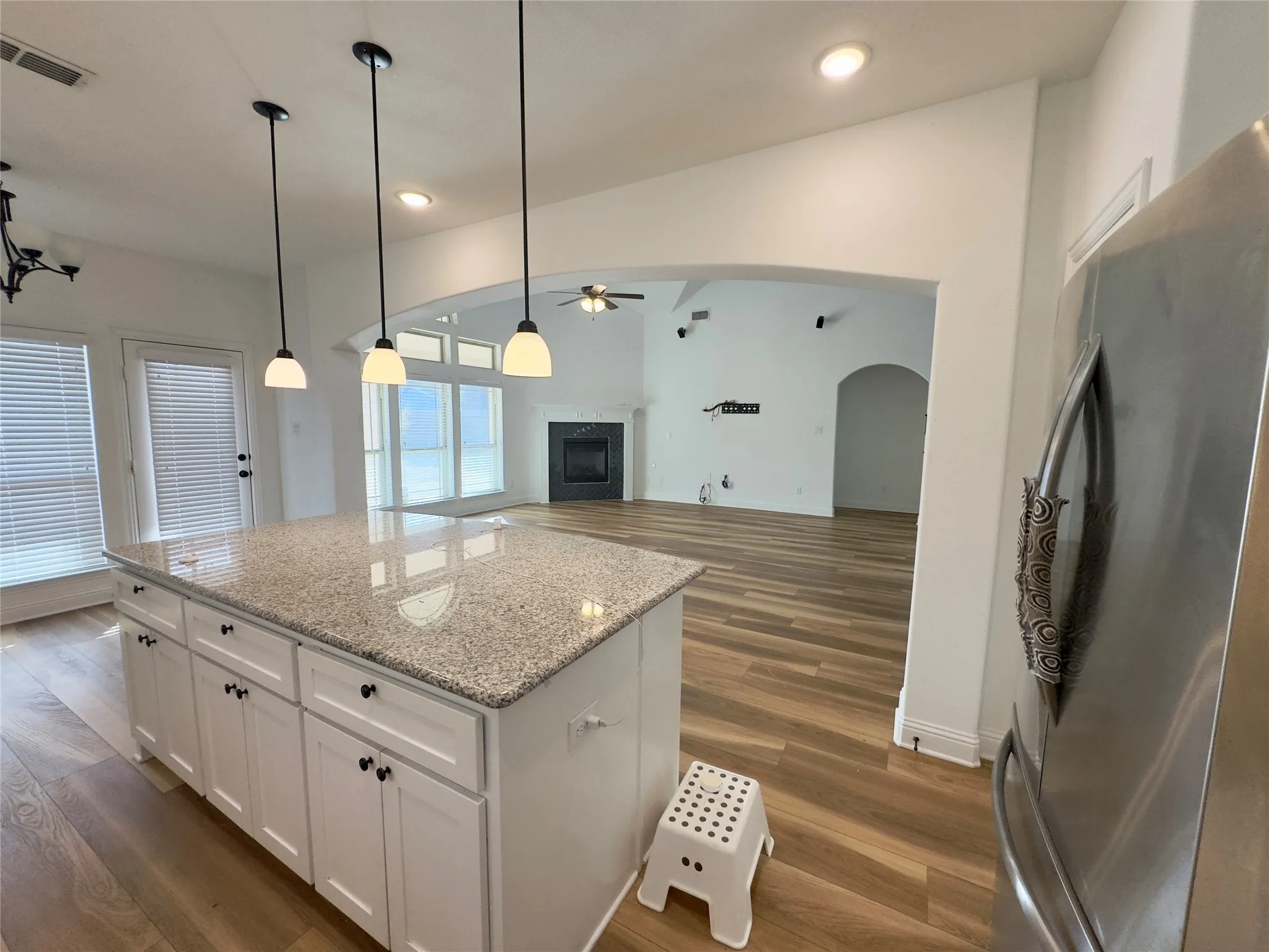 Kitchen featuring white cabinetry, light stone counters, ceiling fan, stainless steel refrigerator, and pendant lighting
