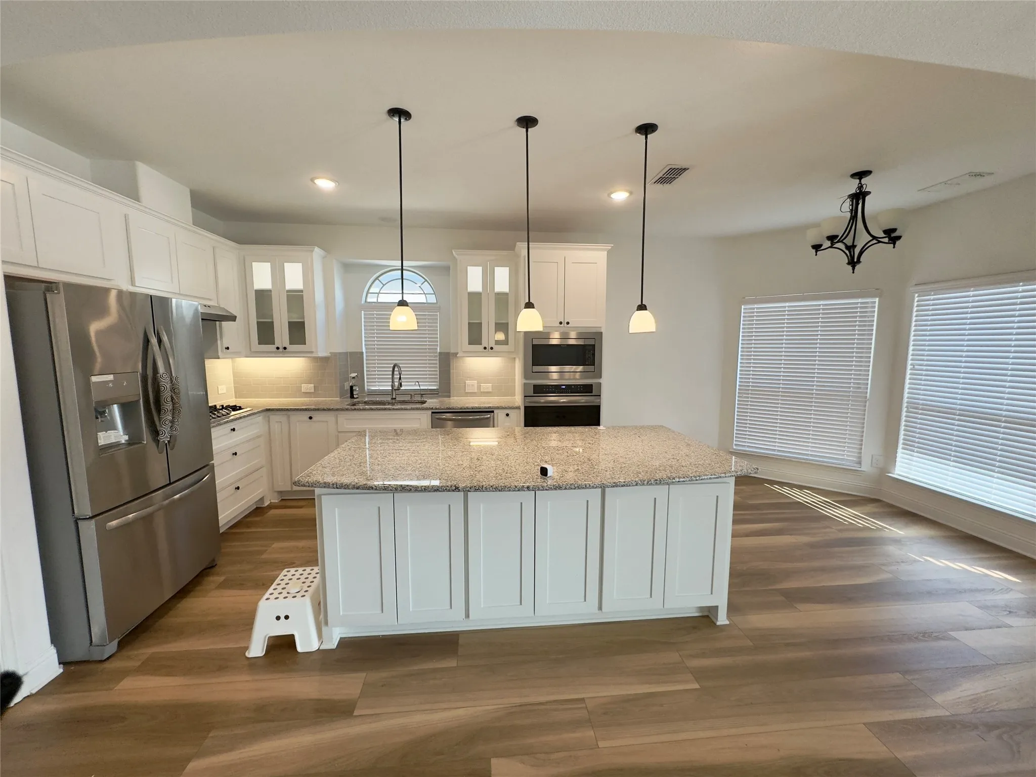 Kitchen featuring pendant lighting, stainless steel appliances, a kitchen island, white cabinetry, and sink