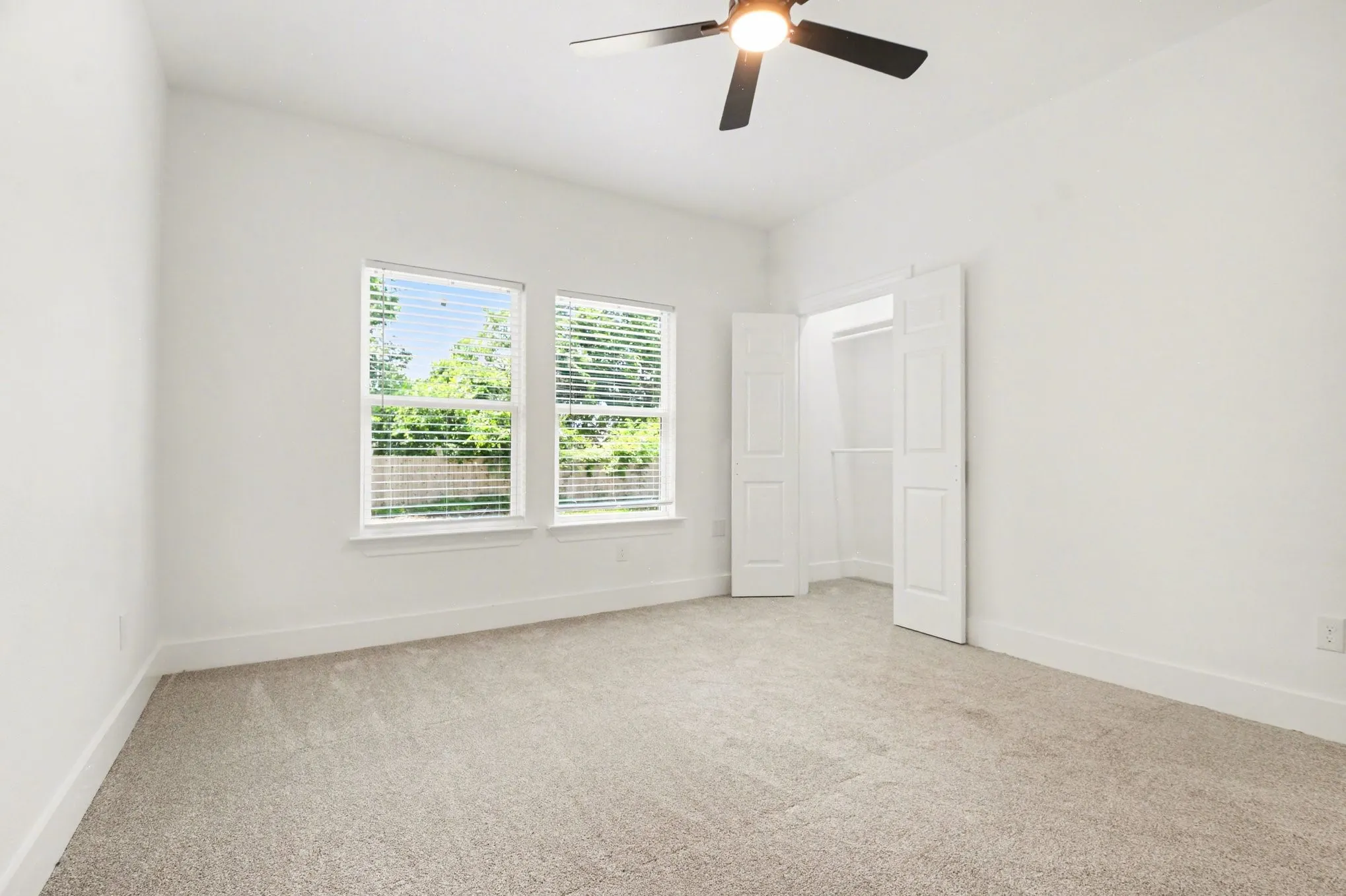 Neutral-toned carpeting, white walls, two windows with blinds, and a ceiling fan with integrated lighting