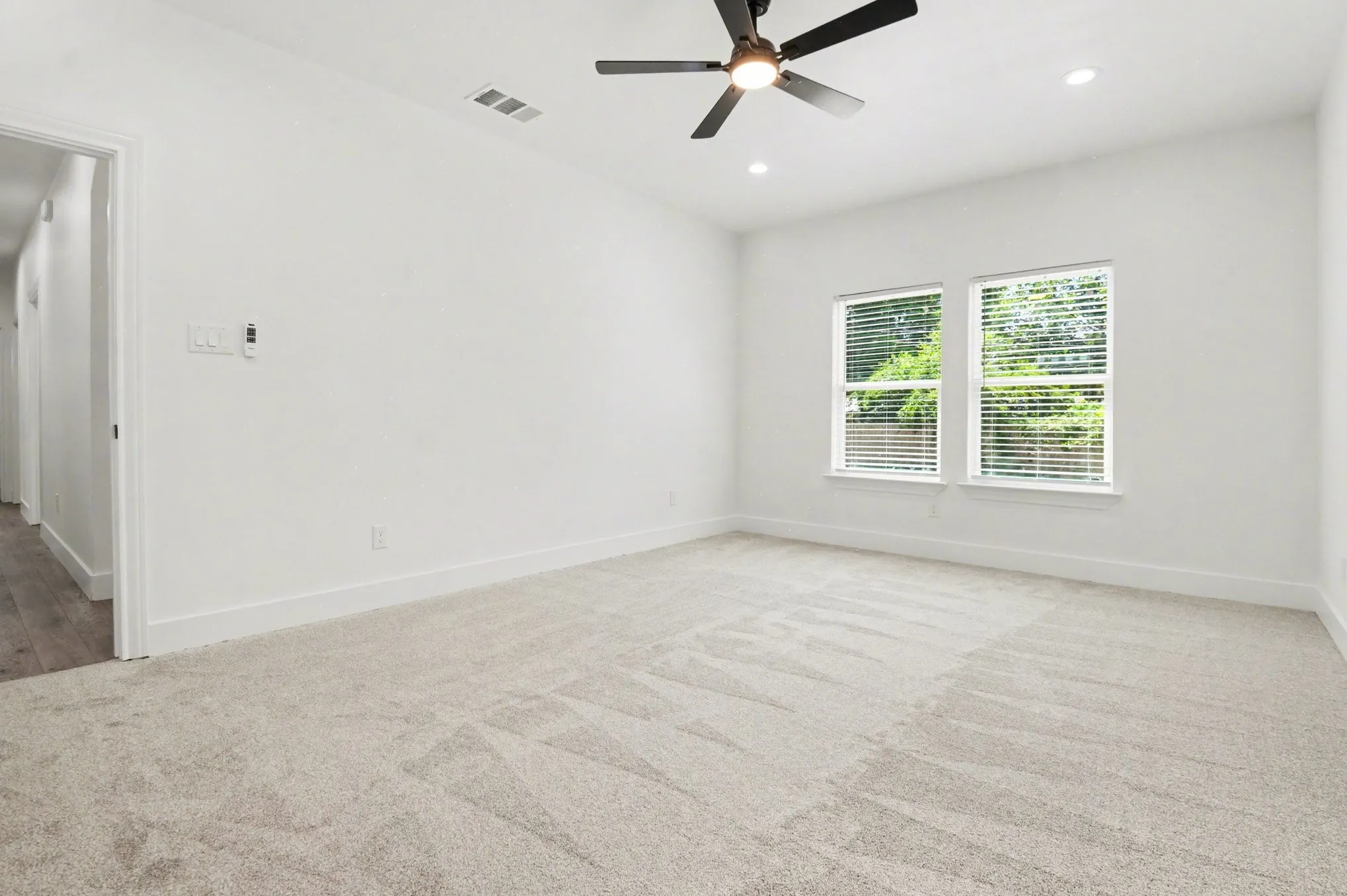 Recessed lighting, ceiling fan, two windows with blinds, light-toned carpet, and a white interior