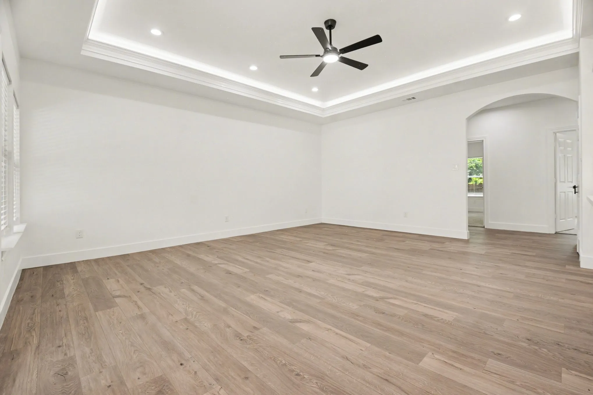 Recessed lighting, tray ceiling, wood-finish flooring, ceiling fan, and arched doorway